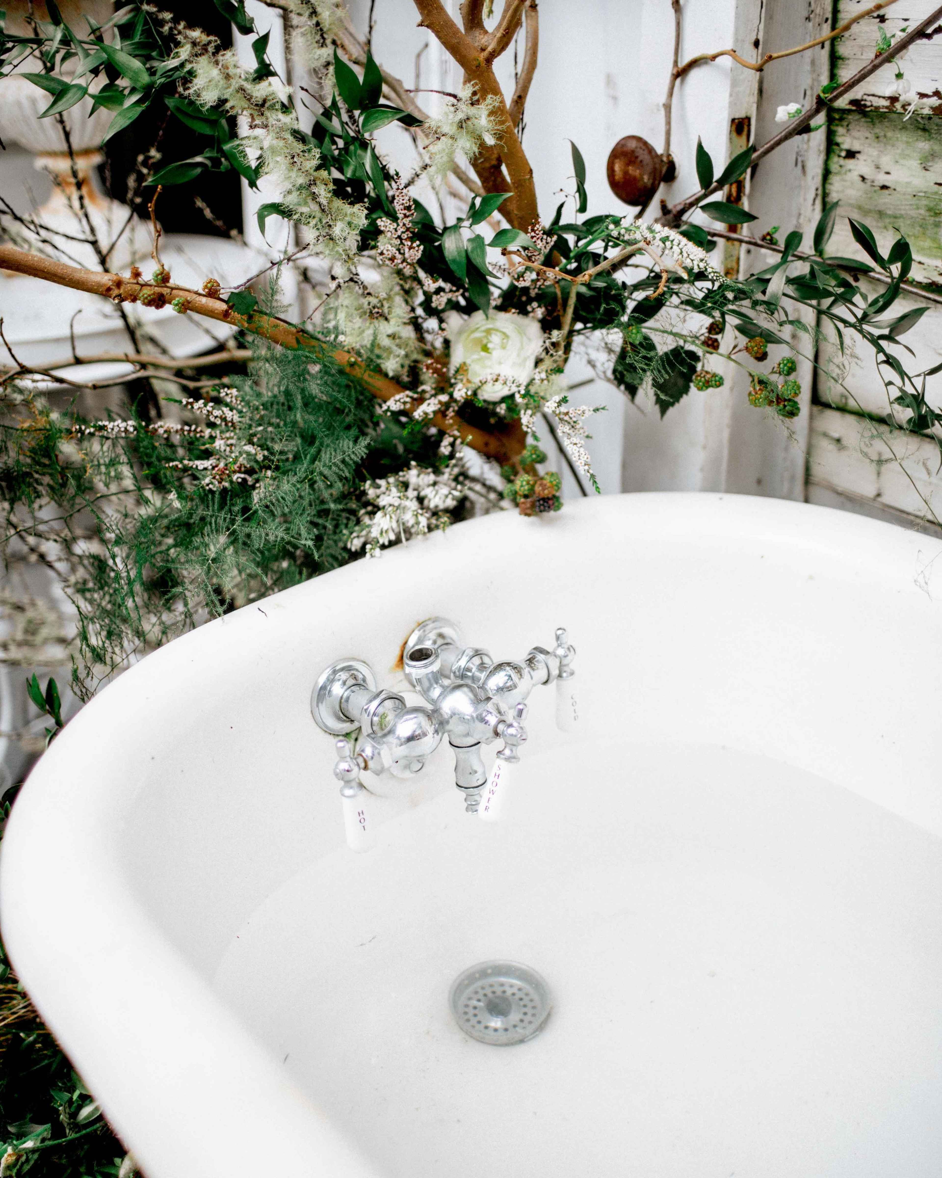 A vintage bathtub is positioned under a decorated arrangement of branches and flowers.