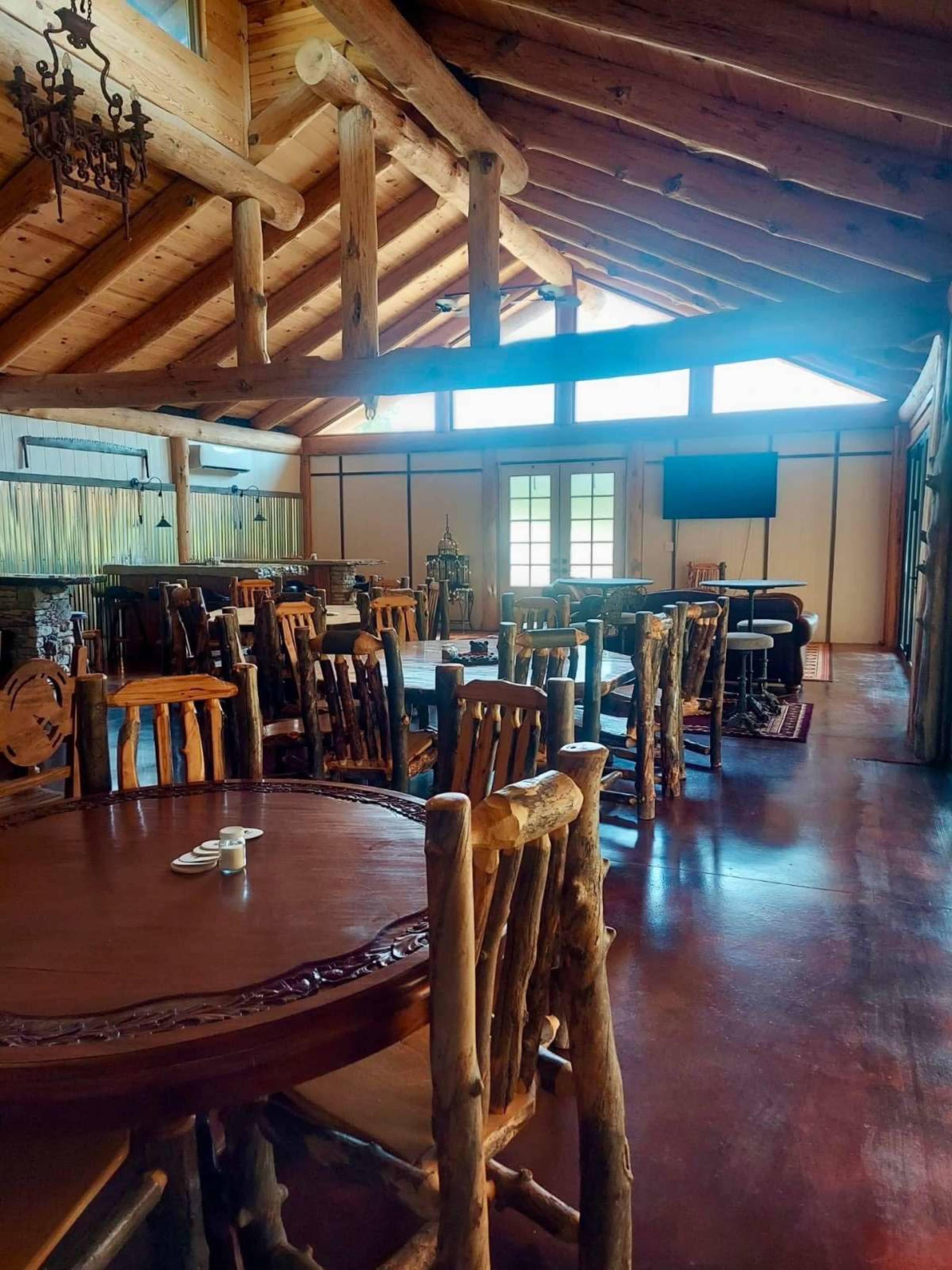 The interior of a rustic lodge features wooden furniture, high ceilings with exposed beams, and large windows allowing natural light.