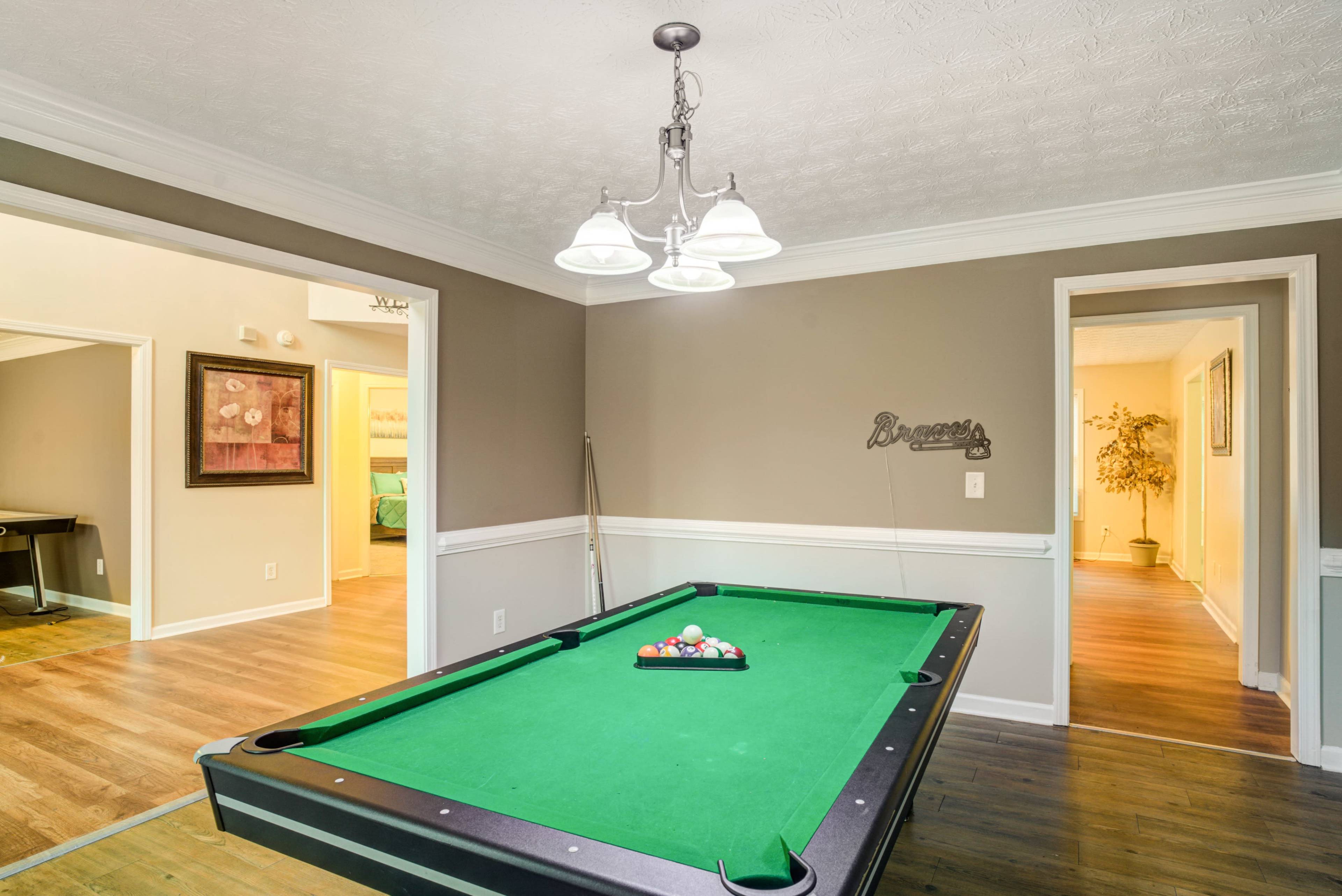 A billiards table is positioned in a well-lit room featuring light walls and doorways leading to adjacent rooms.