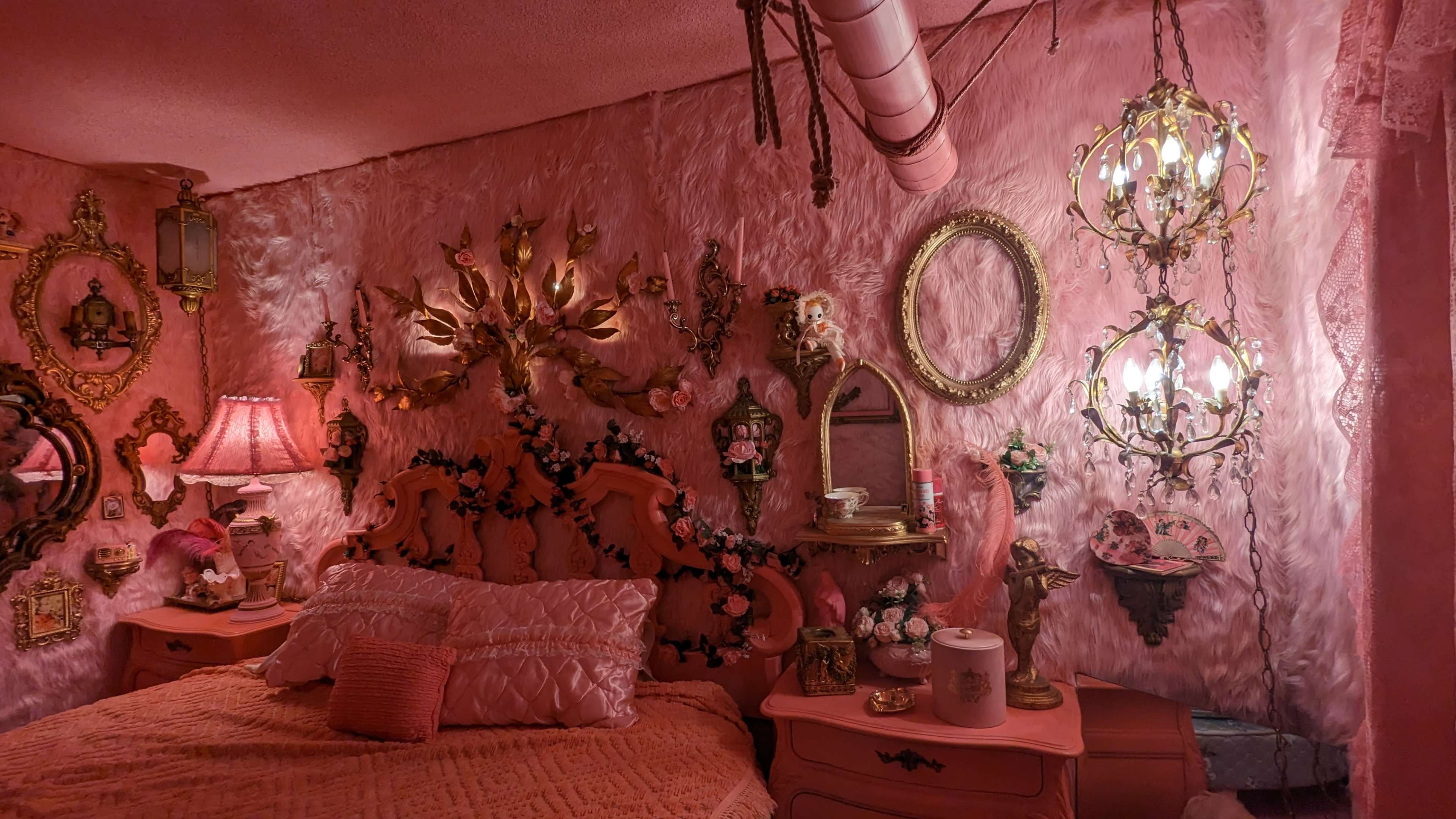 The scene features a pink room with a bed adorned with decorative pillows, surrounded by ornate wall decorations, chandeliers, and a vintage mirror.
