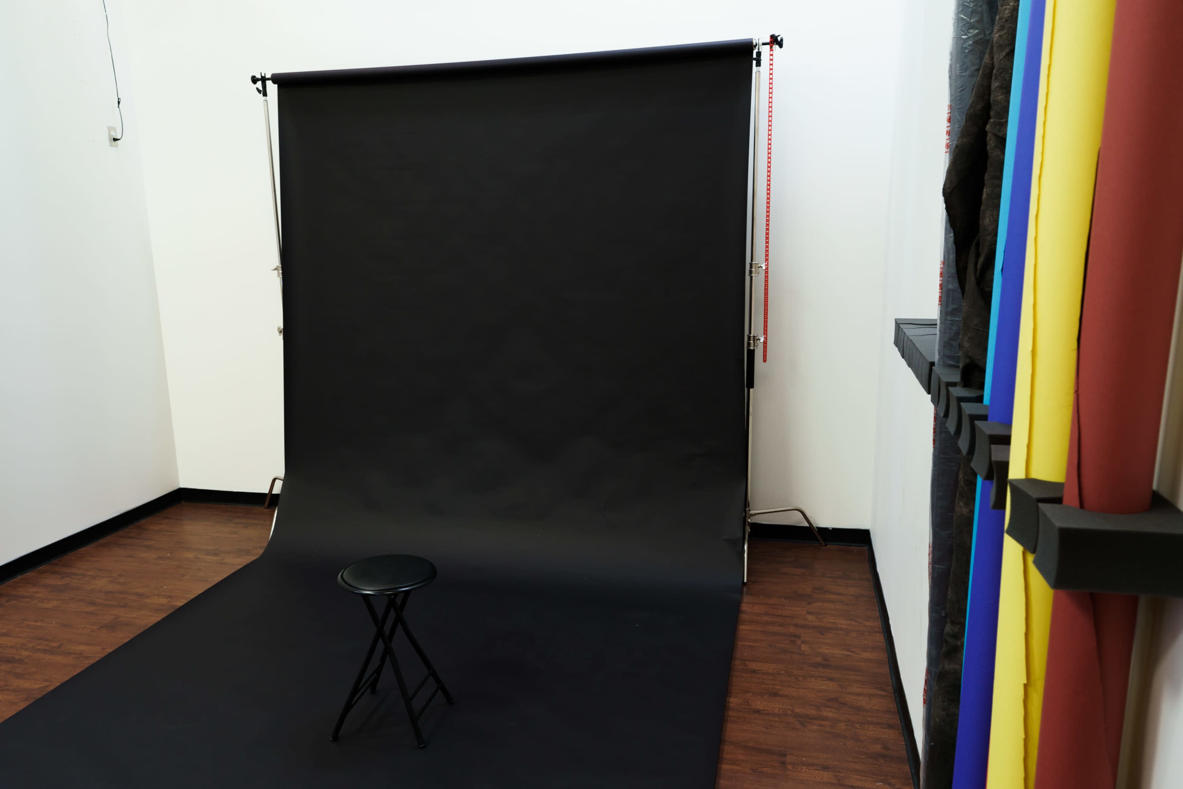 A photography studio with a black backdrop and a single black stool positioned in front of it.
