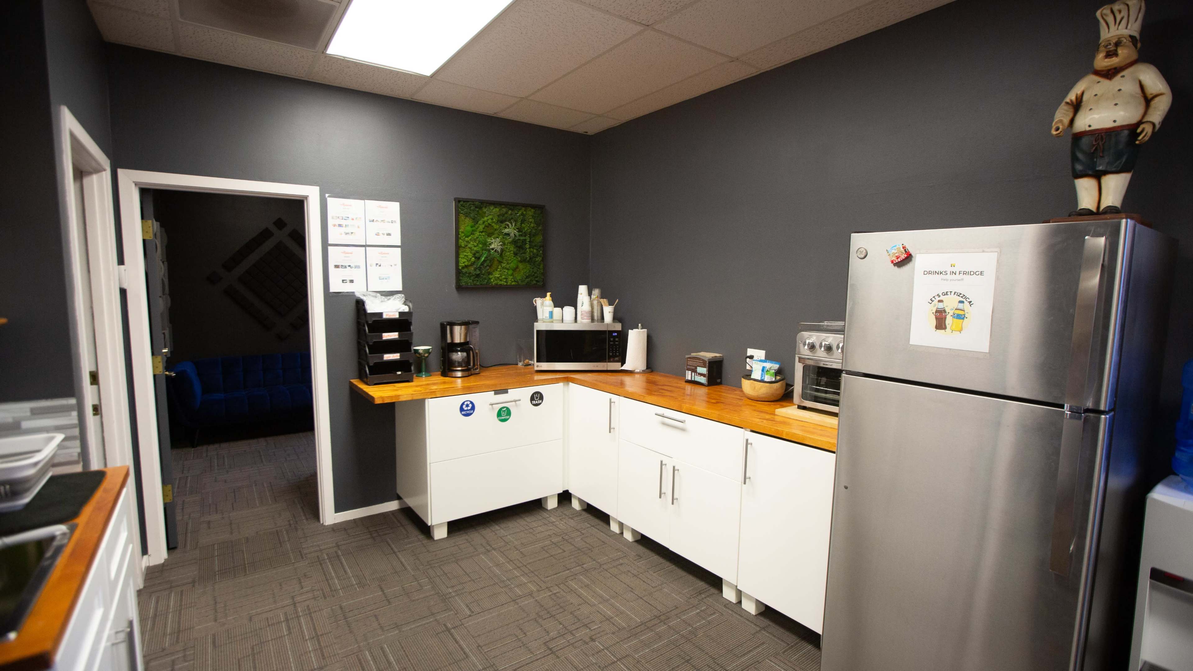 The image shows a kitchen area with a wooden countertop, a stainless steel refrigerator, and various appliances against a gray wall.