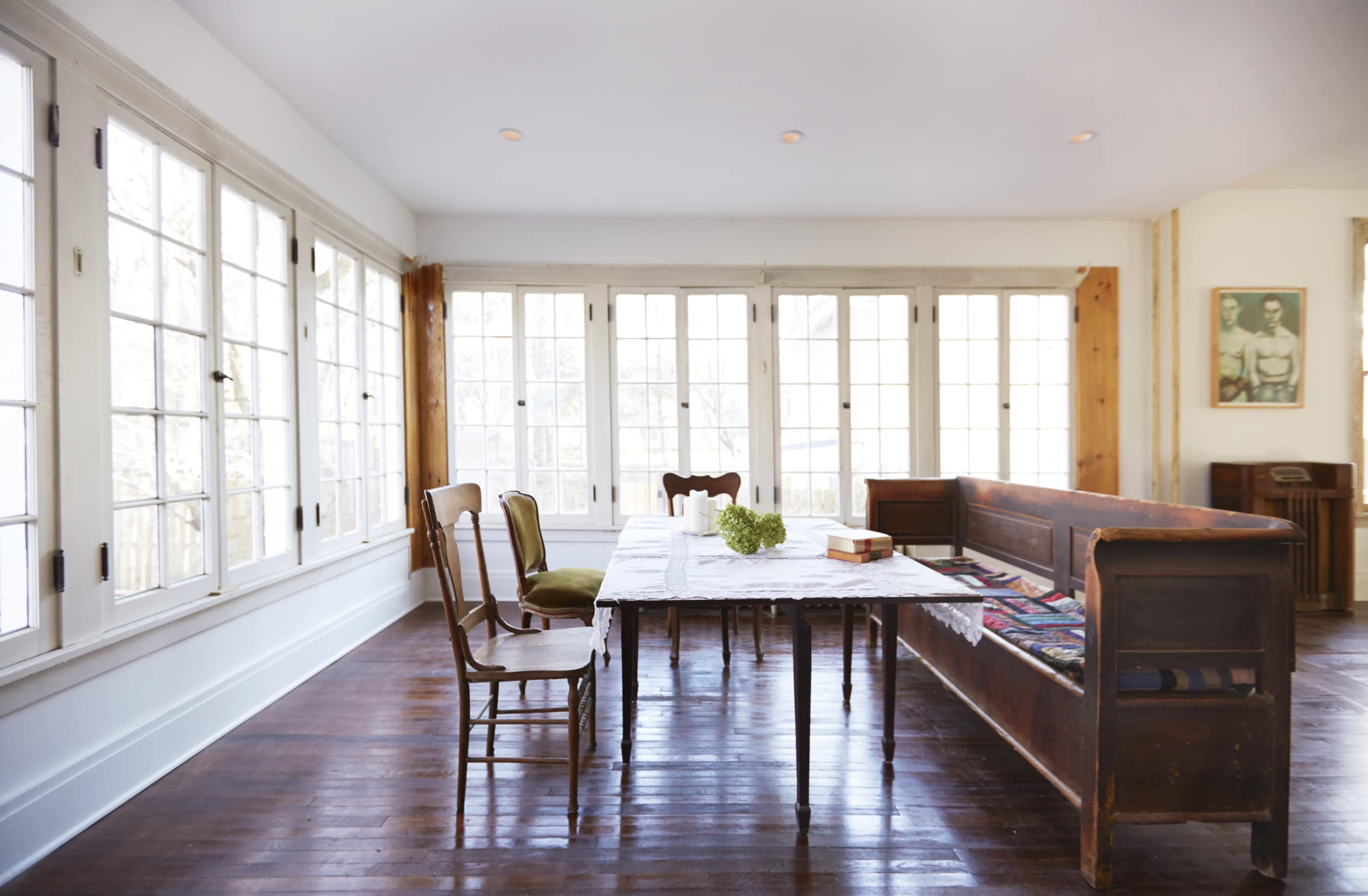 A spacious dining area with a large table and a mix of wooden chairs, surrounded by multiple windows that provide ample natural light.