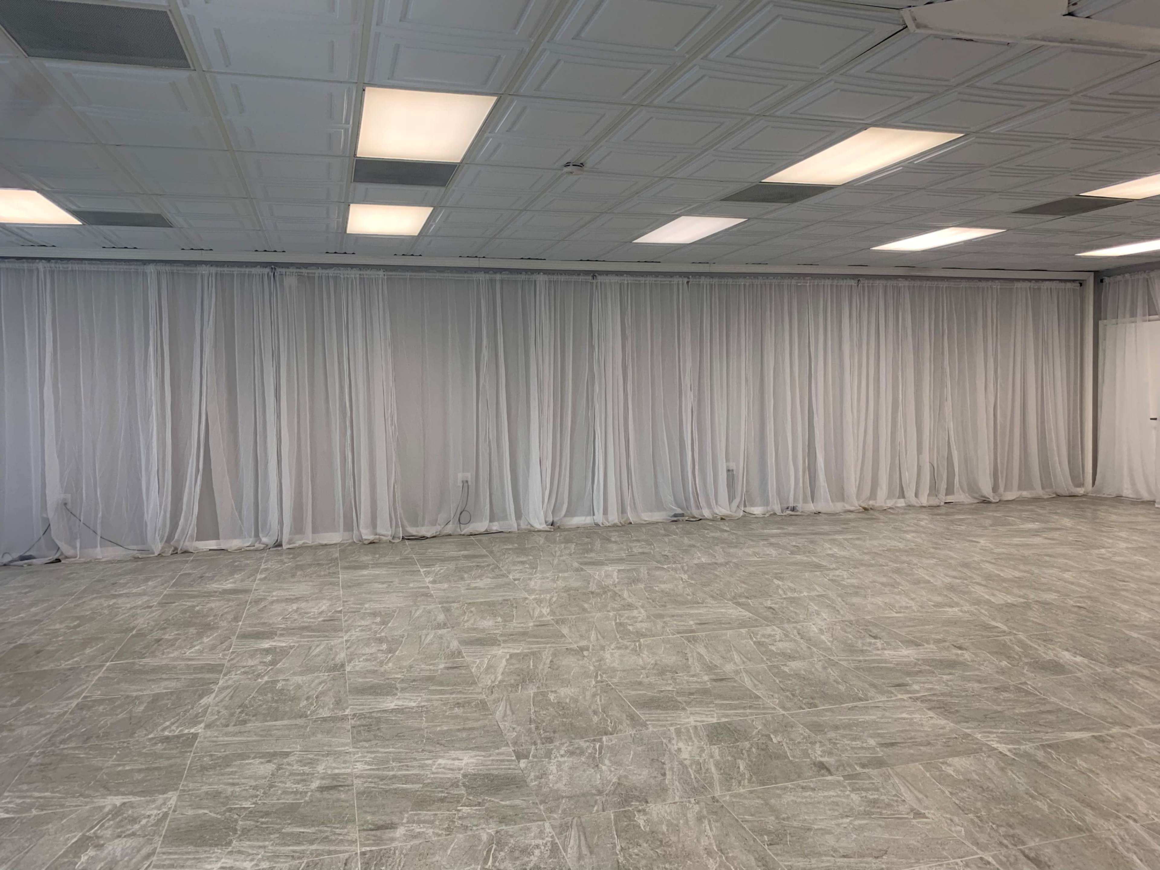 A spacious room with white draped curtains and a tiled gray floor.