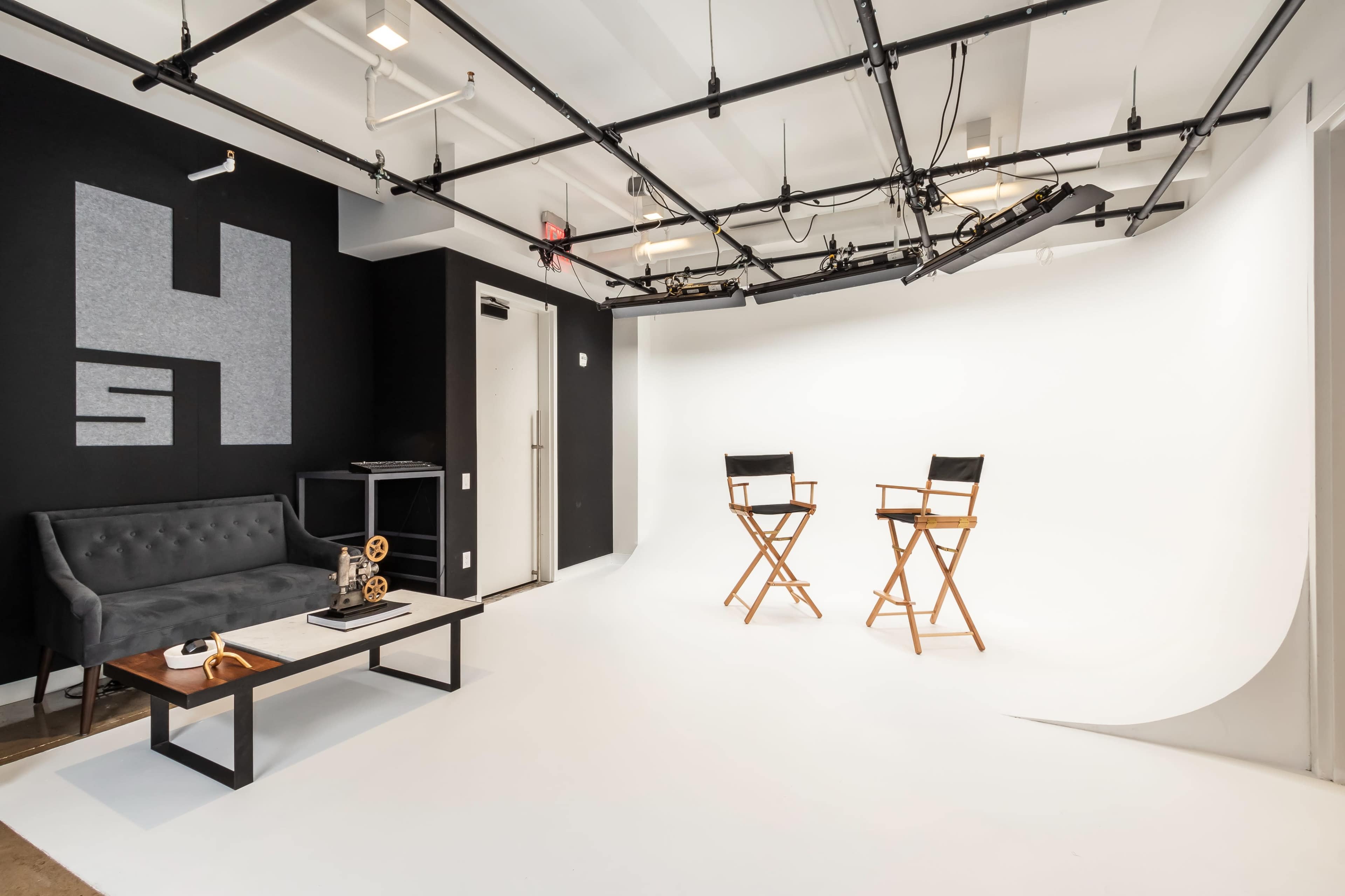 A minimalist studio space featuring two director's chairs in front of a white backdrop, accompanied by a black couch and a coffee table.