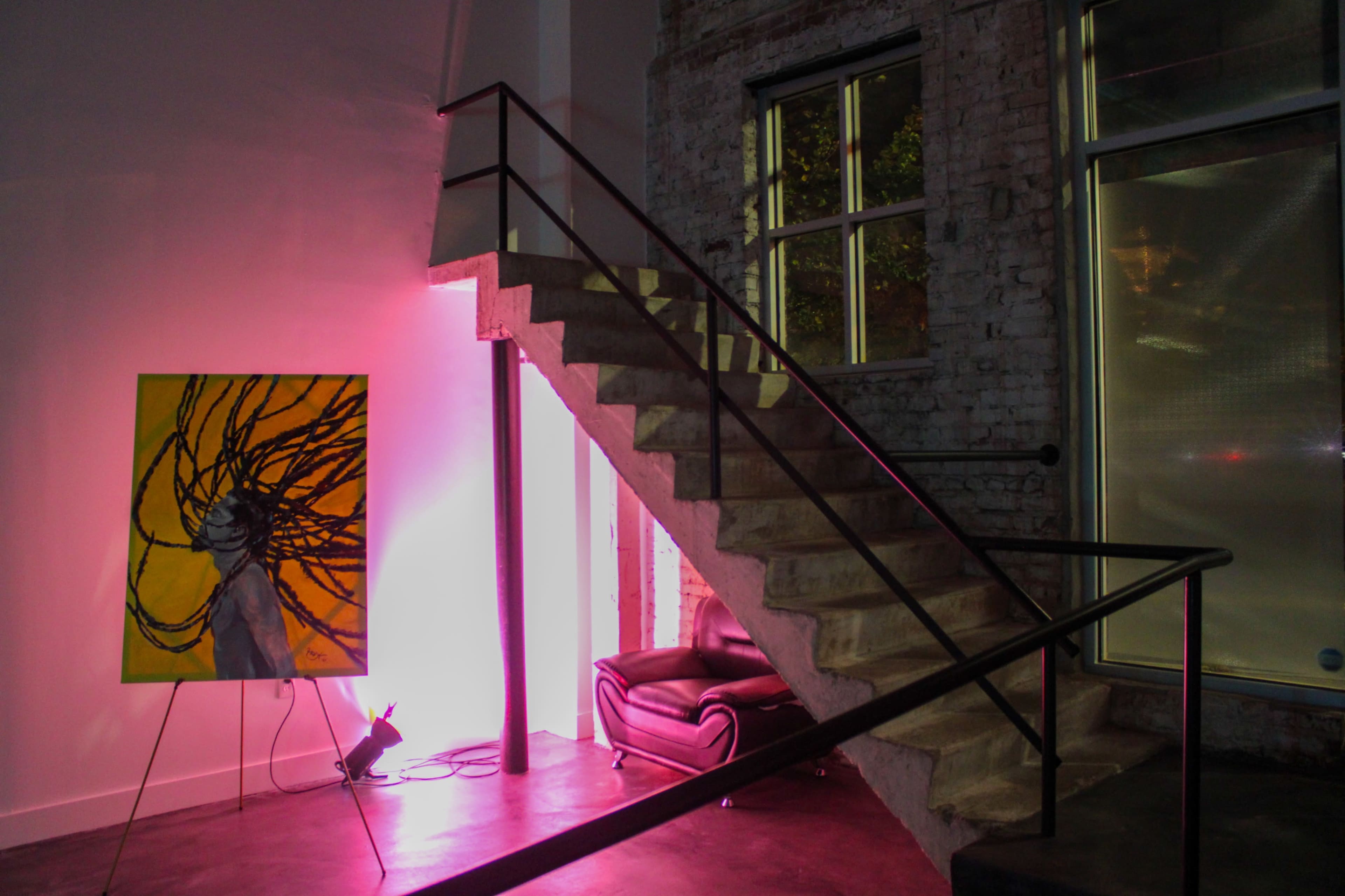 The image shows a lit interior space featuring a staircase with a railing beside a colorful painting on a stand.