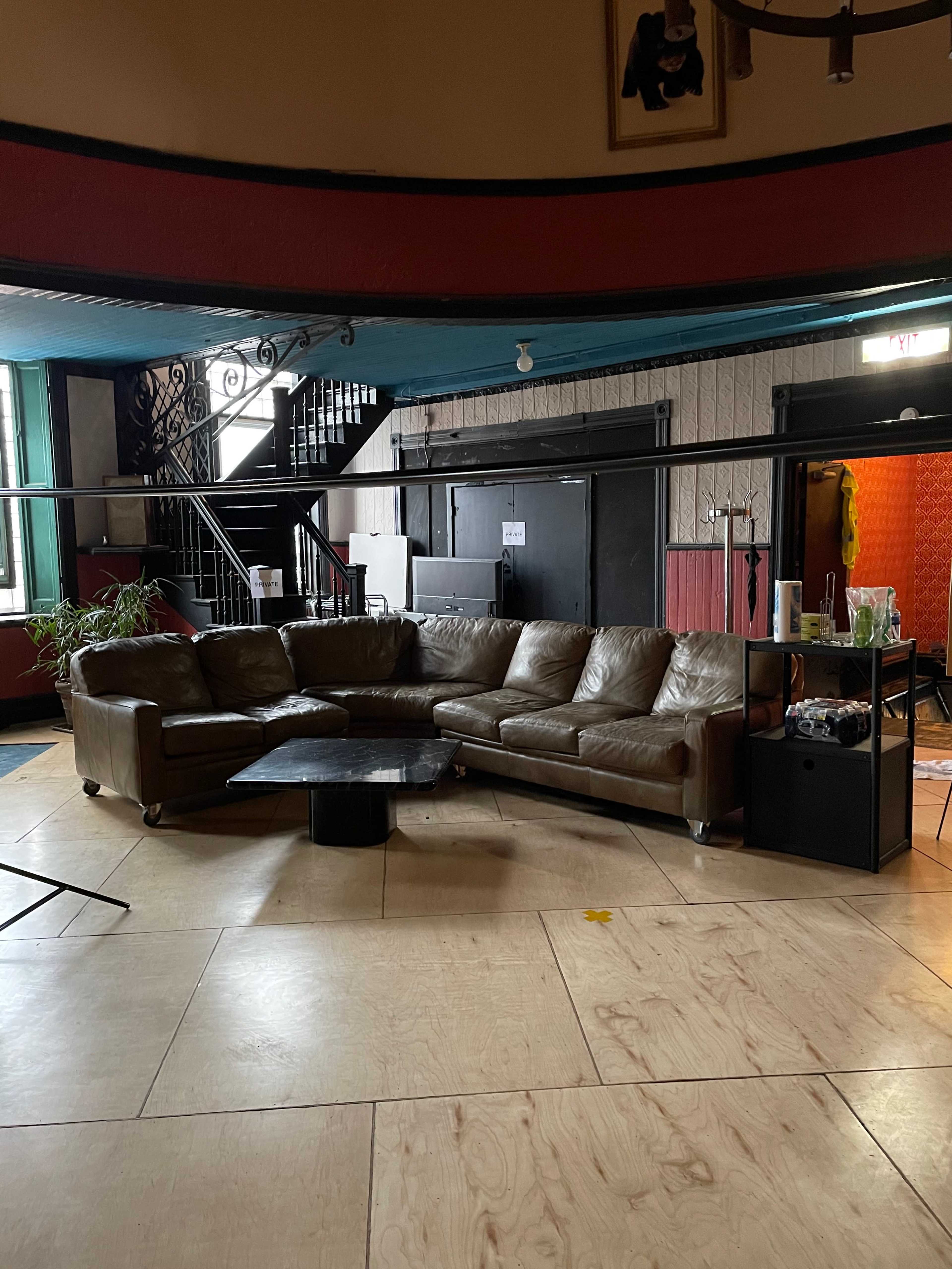 A brown sectional sofa with a black coffee table in a spacious room that features wooden flooring and a staircase in the background.