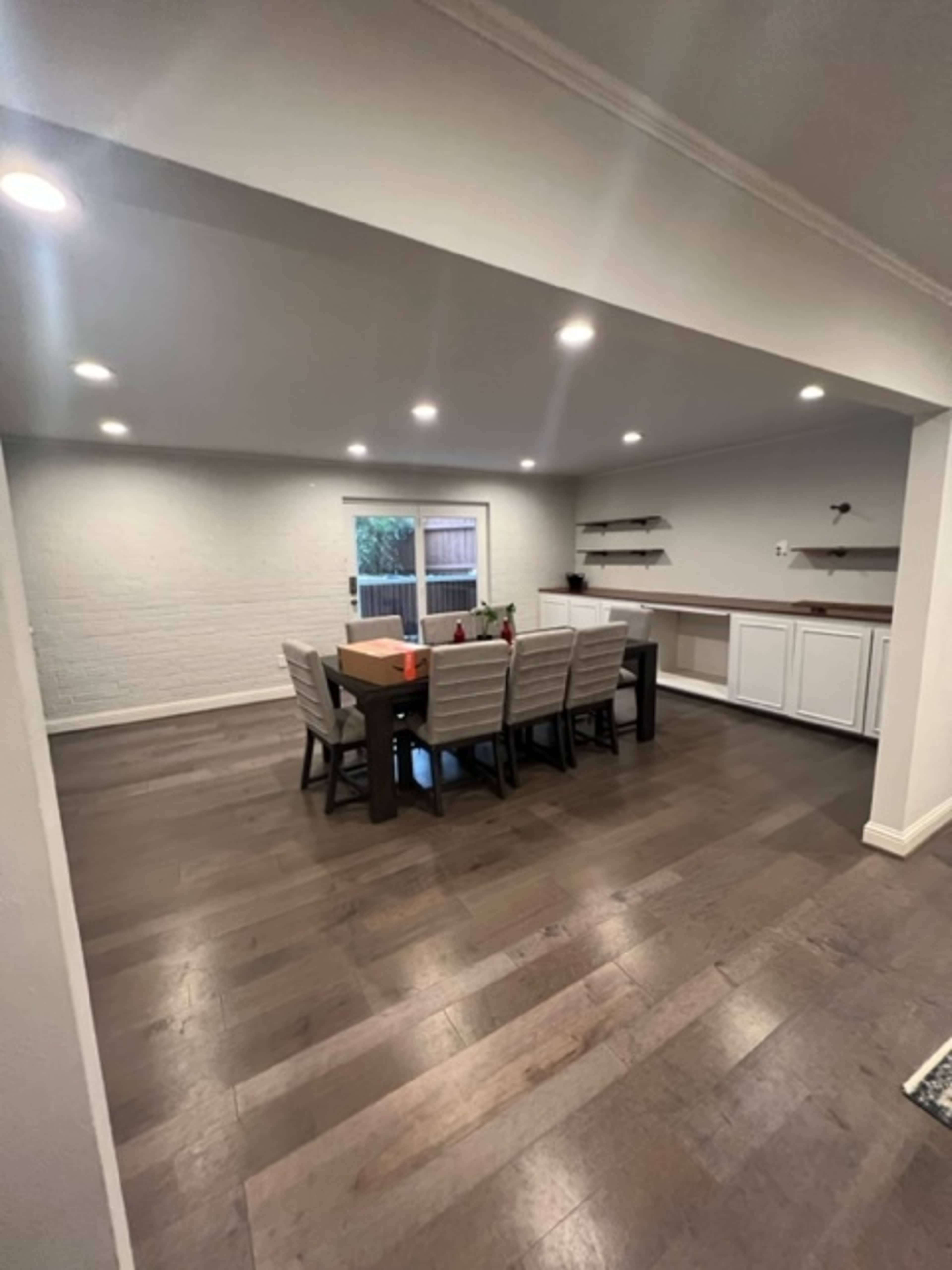 A spacious dining area features a large table surrounded by chairs, with a sliding glass door that opens to an outdoor space.