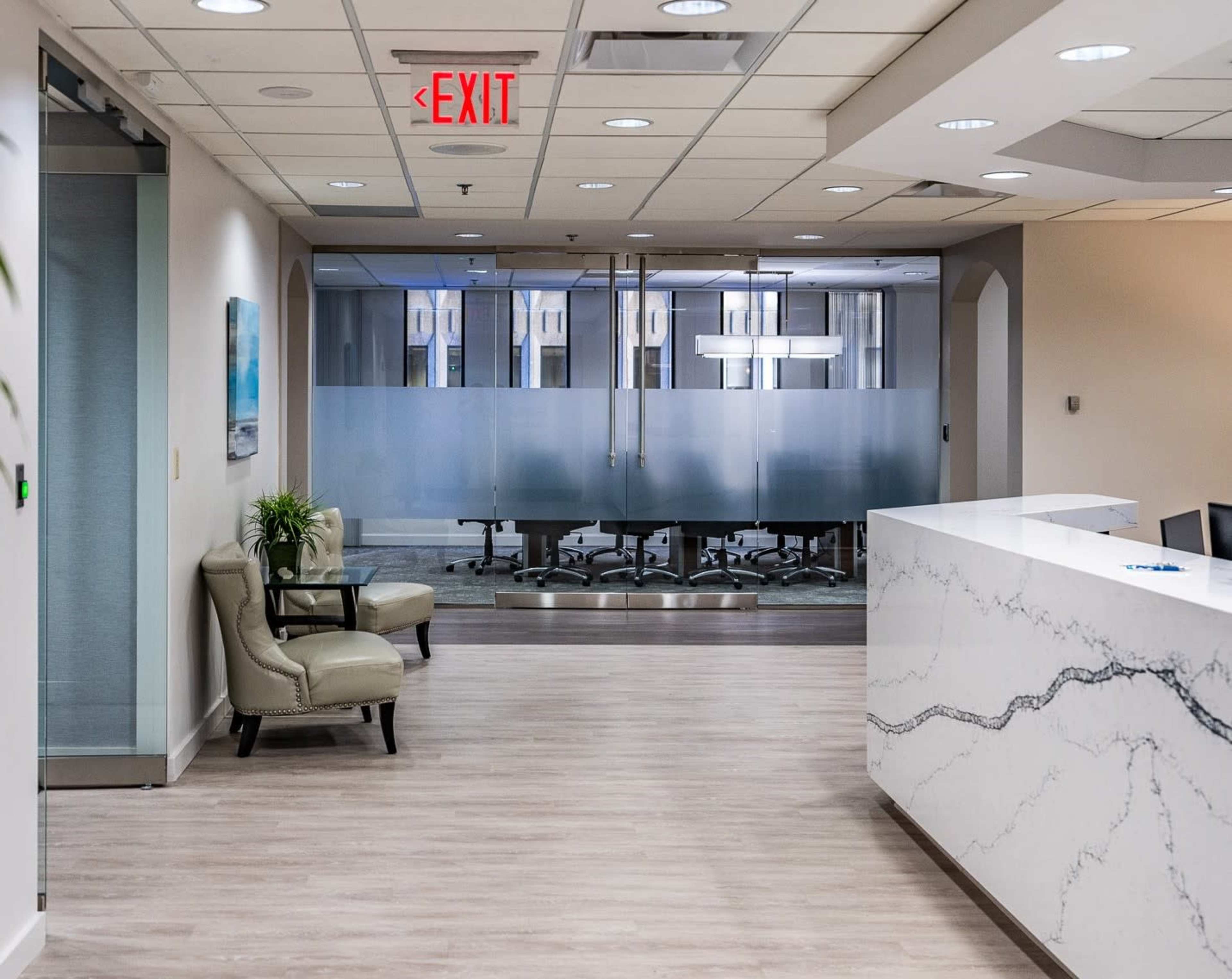 The image shows a well-lit office reception area with a marble front desk, seating for visitors, and a glass meeting room in the background.