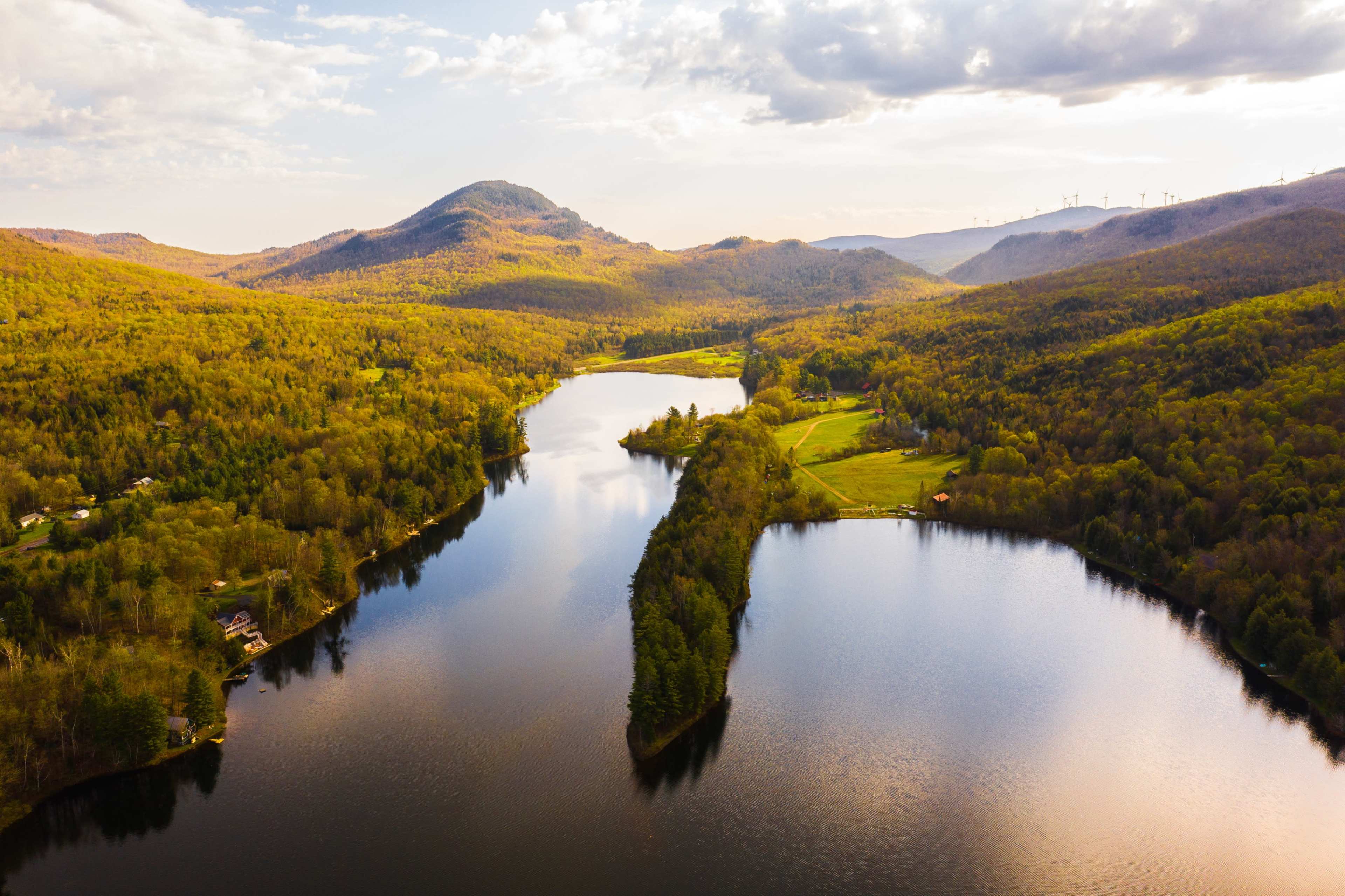 Aerial view of a winding river surrounded by lush green hills and a mountainous backdrop.