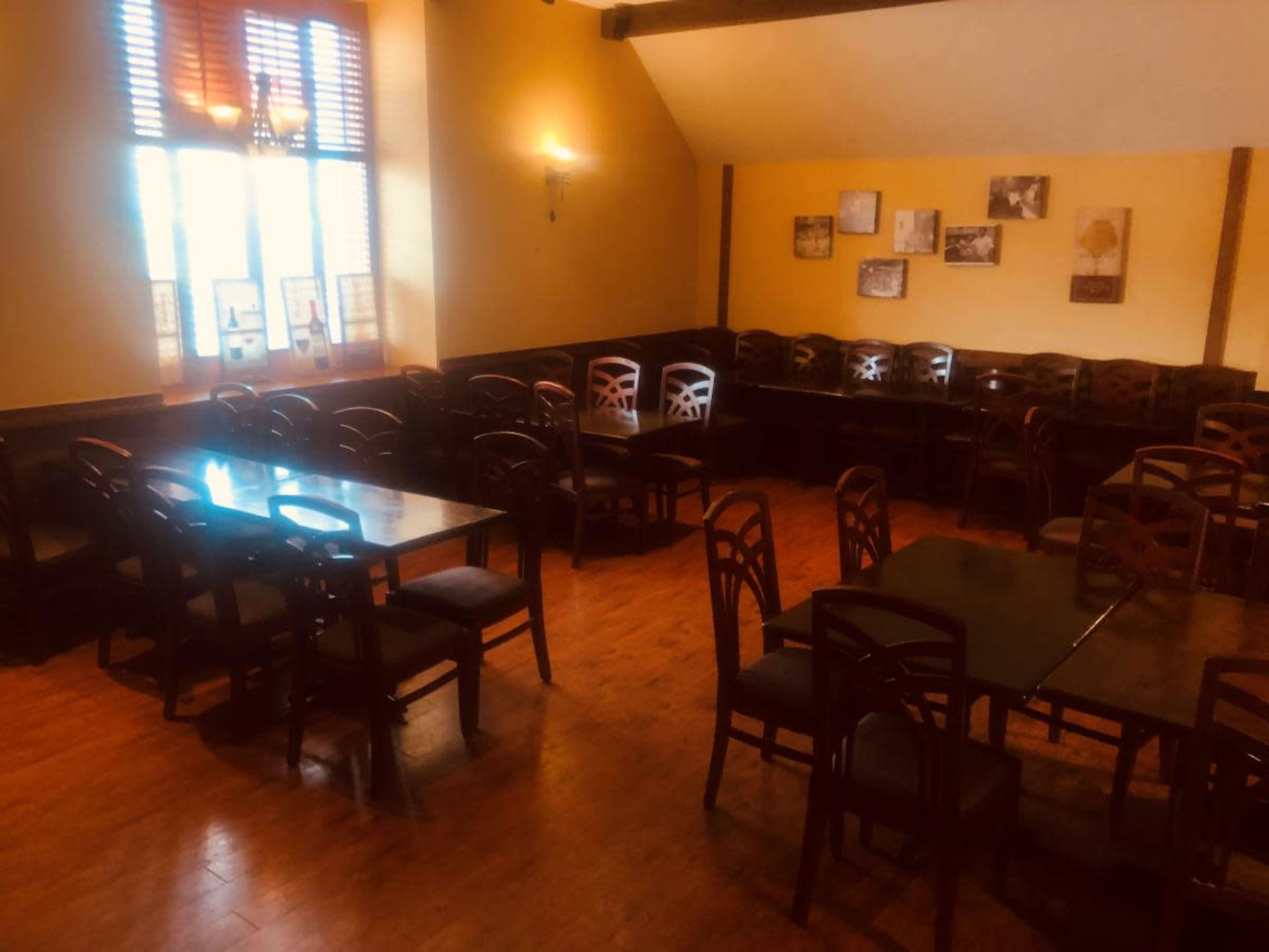A dimly lit restaurant interior with several wooden tables and chairs arranged in a spacious layout.