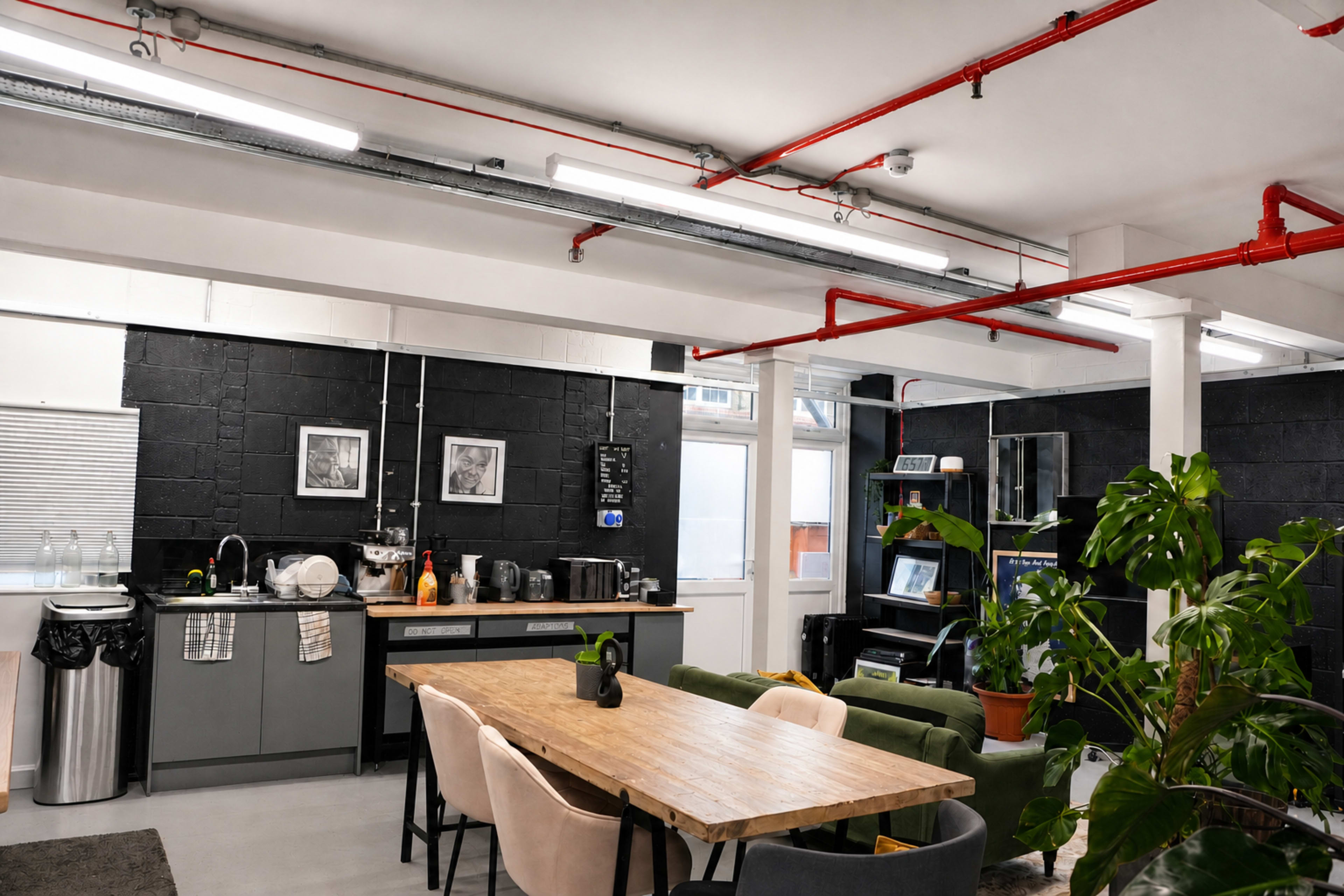 The image shows a modern kitchen and dining area with a long wooden table, green chairs, and industrial-style features such as exposed pipes and black walls.