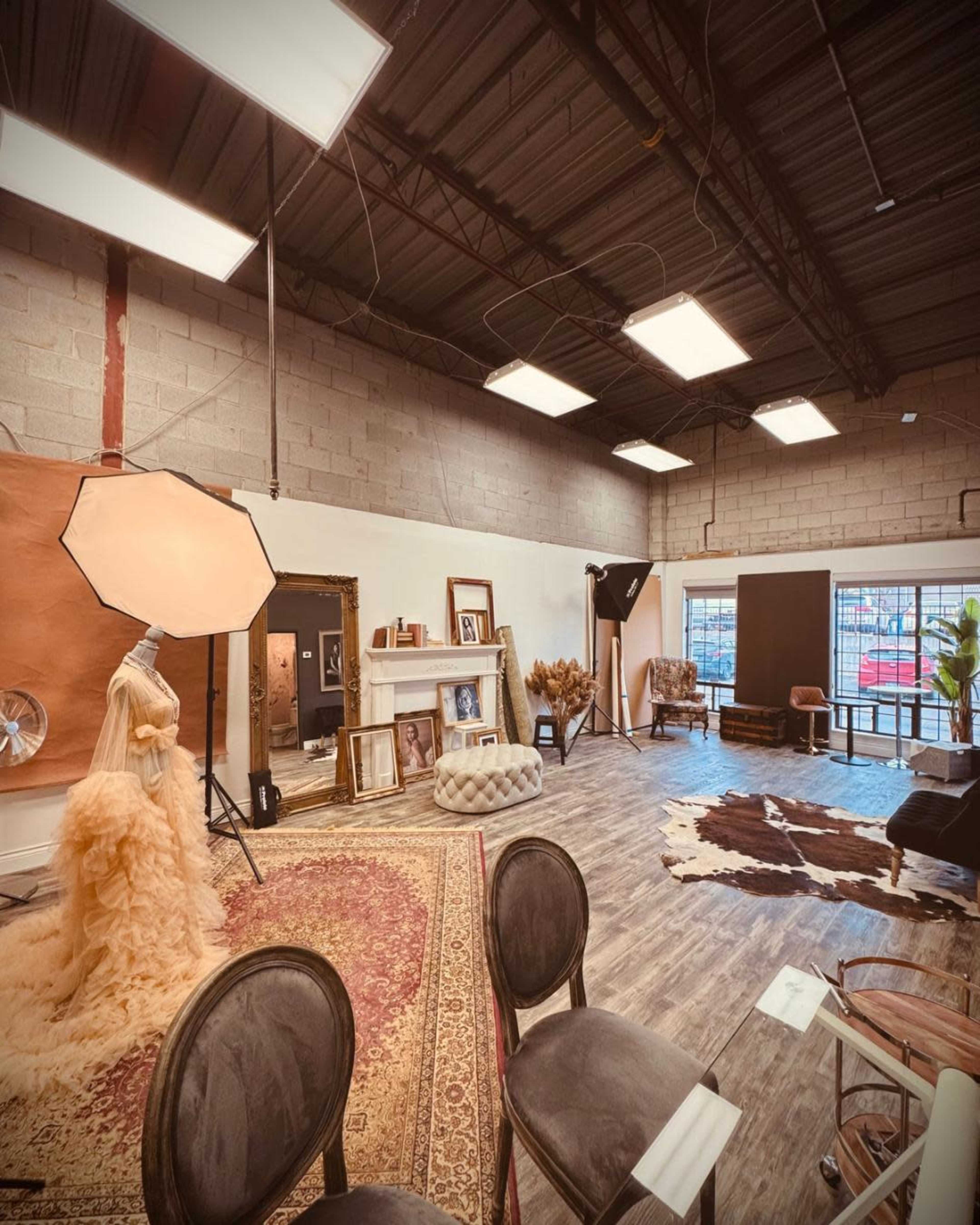 The image shows a spacious studio with a large backdrop, photography equipment, a vintage-style rug, and various decorative elements.