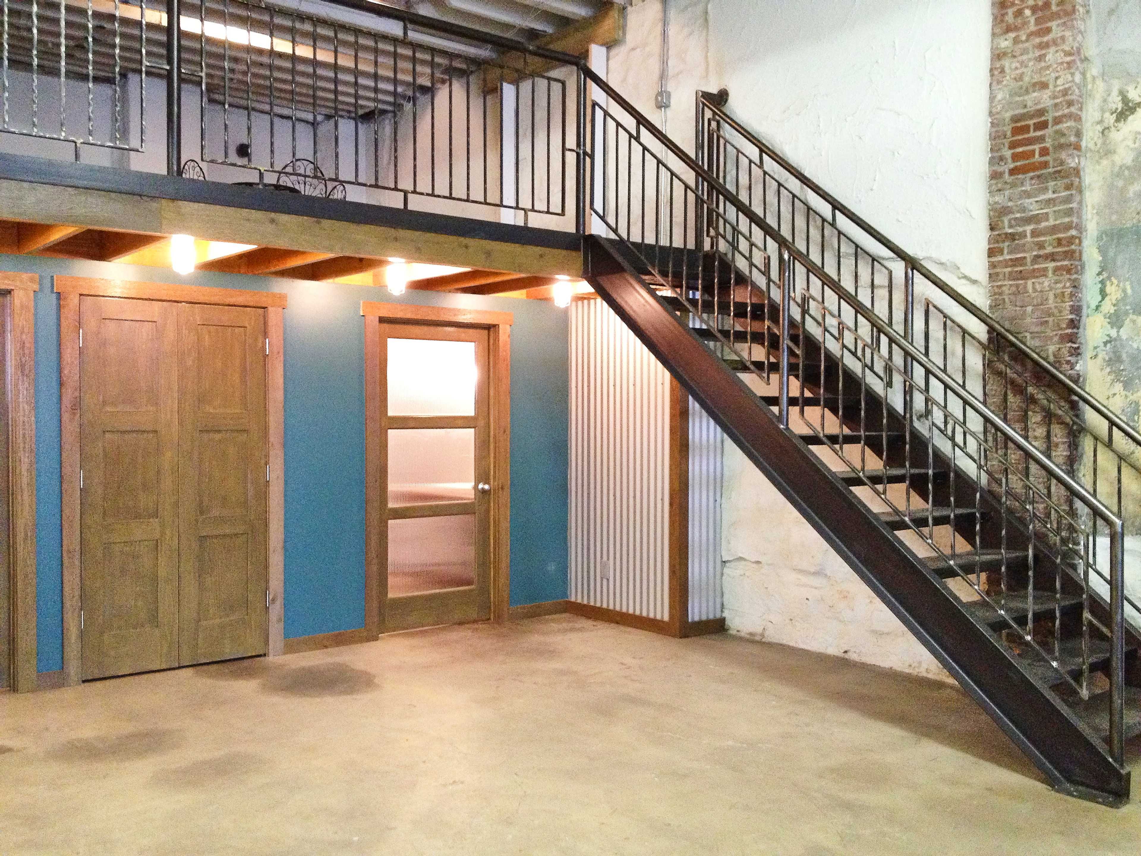 The image shows a spacious interior featuring a staircase on the right, a door on the left, and a blue accent wall in an industrial-style setting.