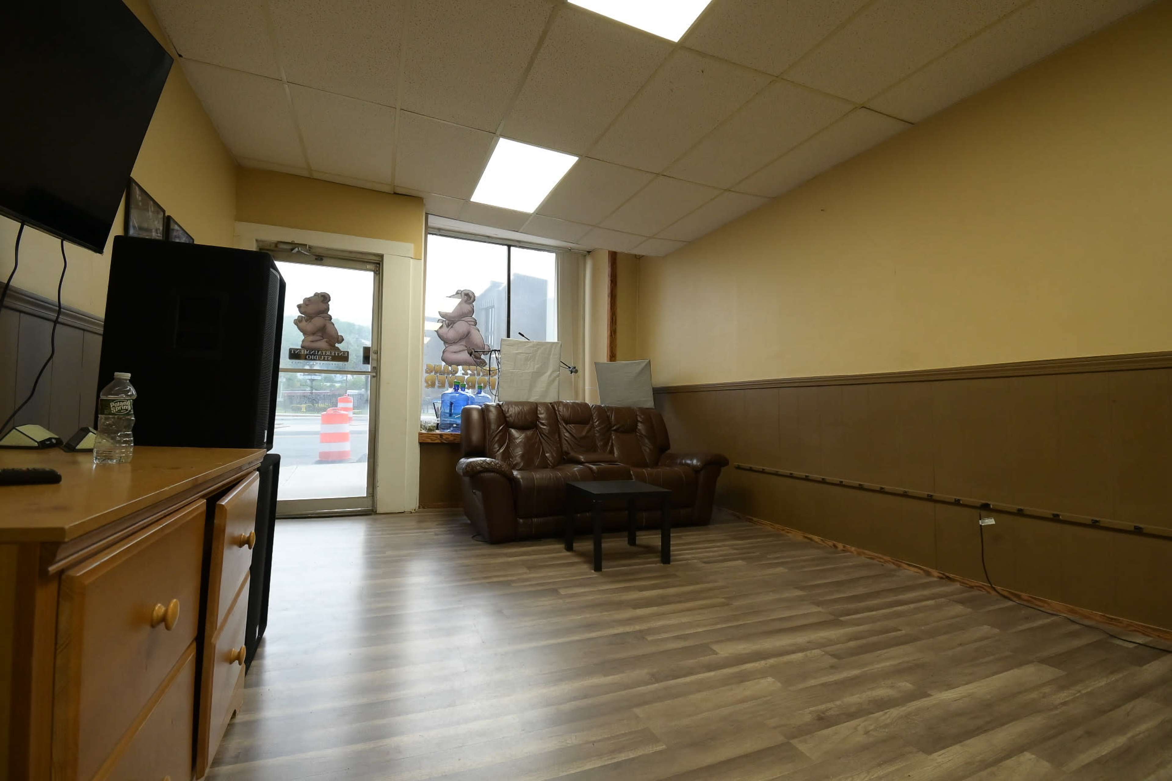 The image shows a sparsely furnished room with a brown leather couch, a small black table, and a door leading outside.