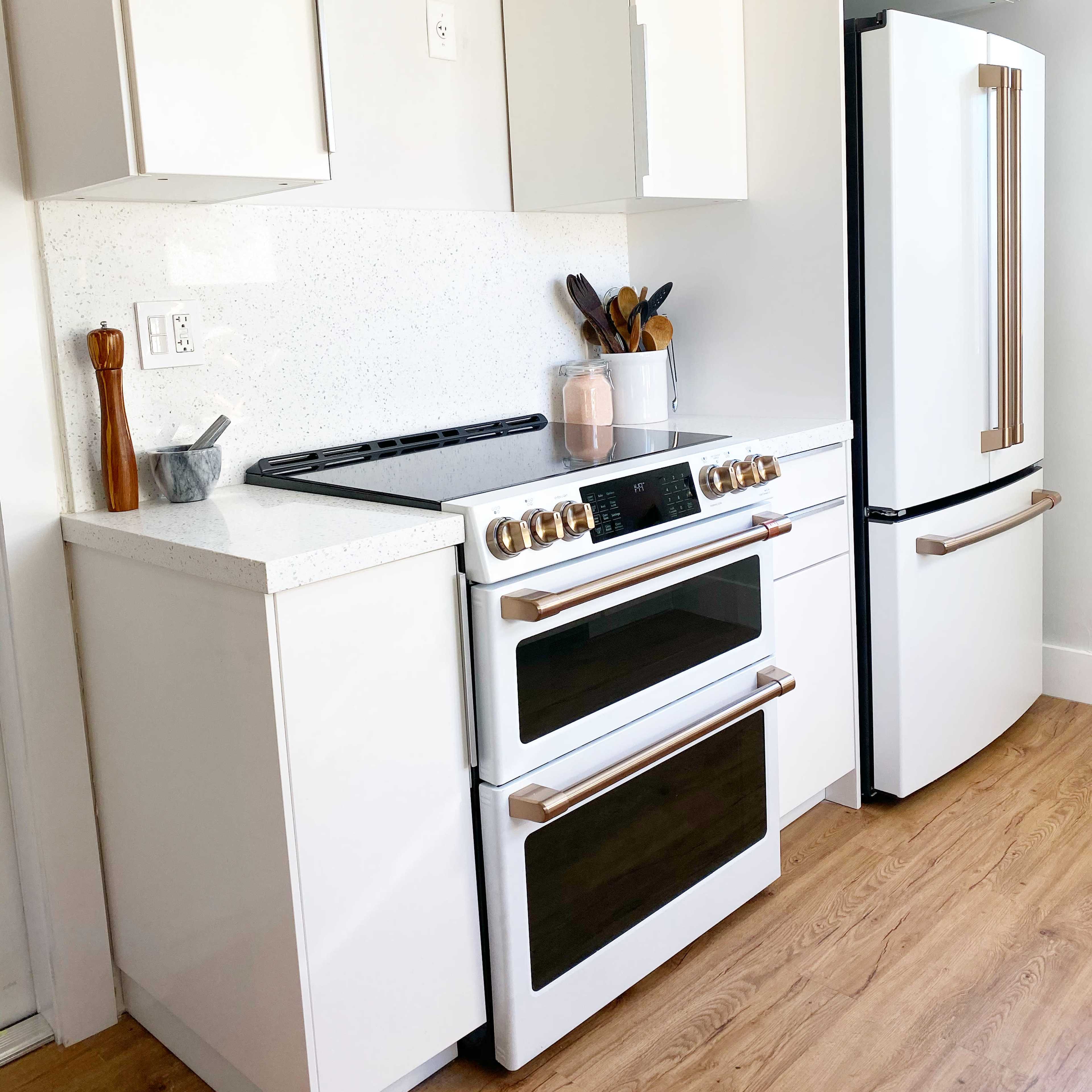 A modern kitchen with a white layout featuring an oven with two compartments, a stovetop, and a refrigerator.
