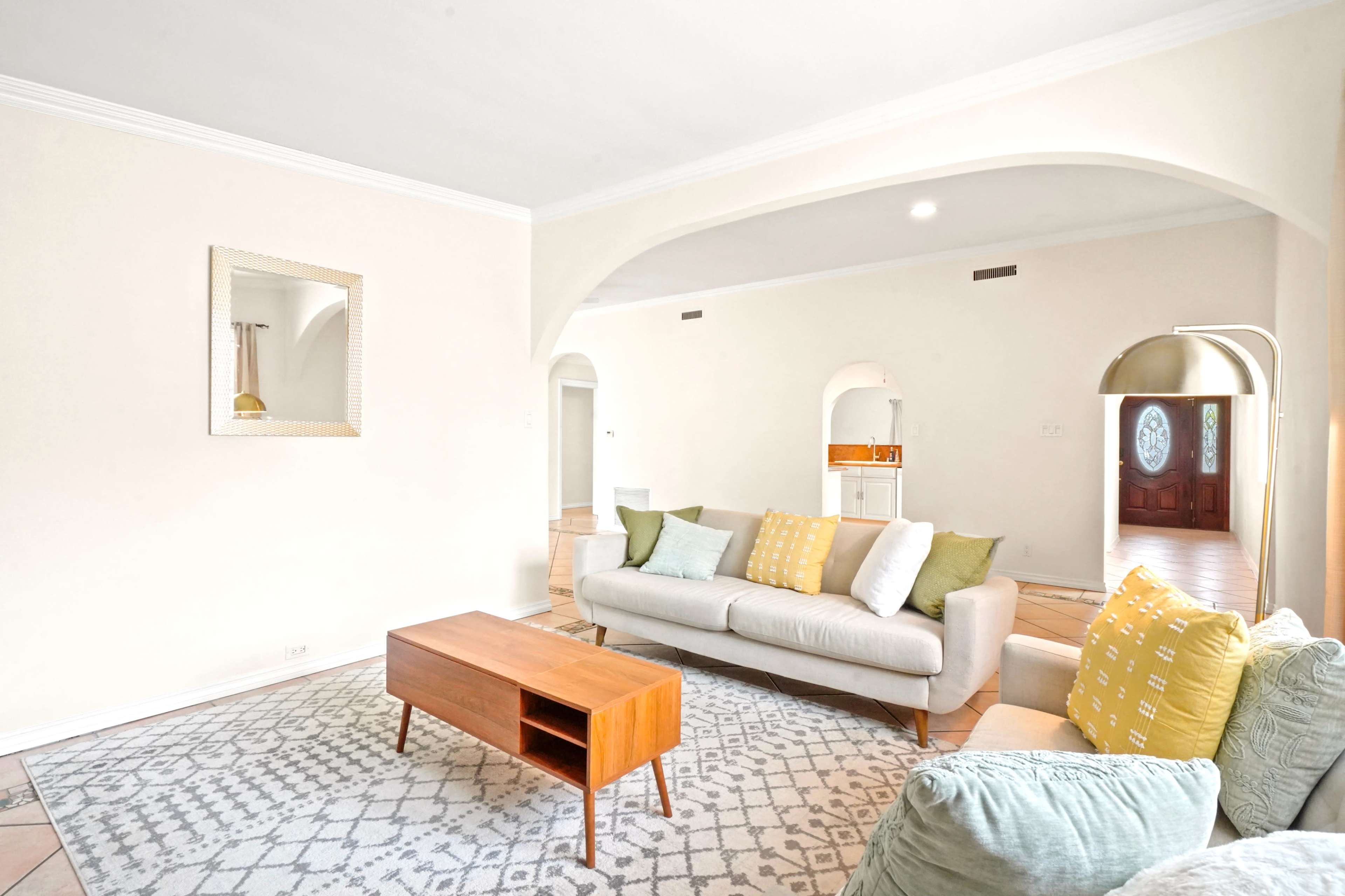A spacious living room featuring a light-colored sofa with decorative pillows, a wooden coffee table, and an archway leading to another room.