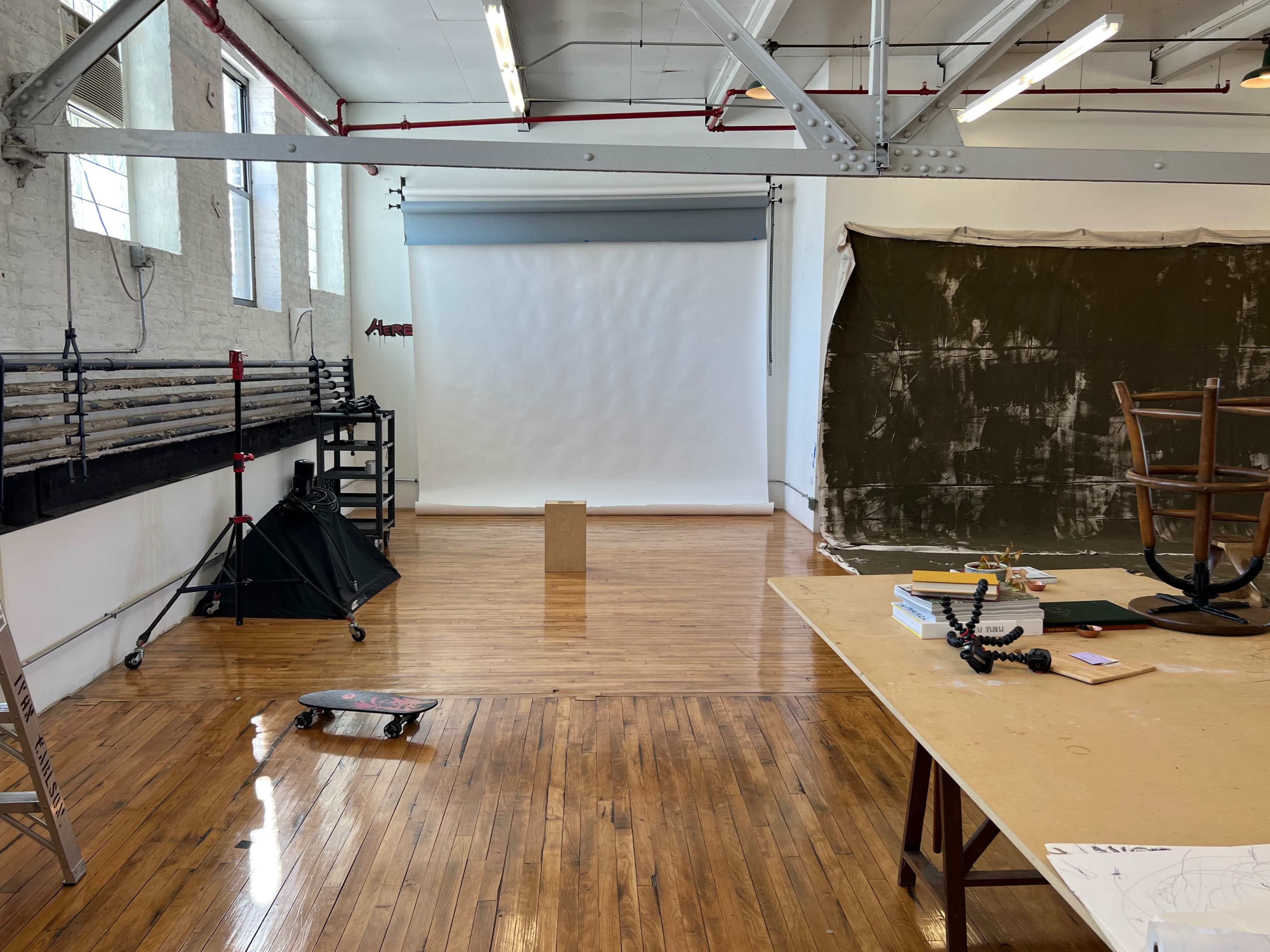 A spacious photography studio with wooden floors, a backdrop setup, and various equipment arranged around the room.