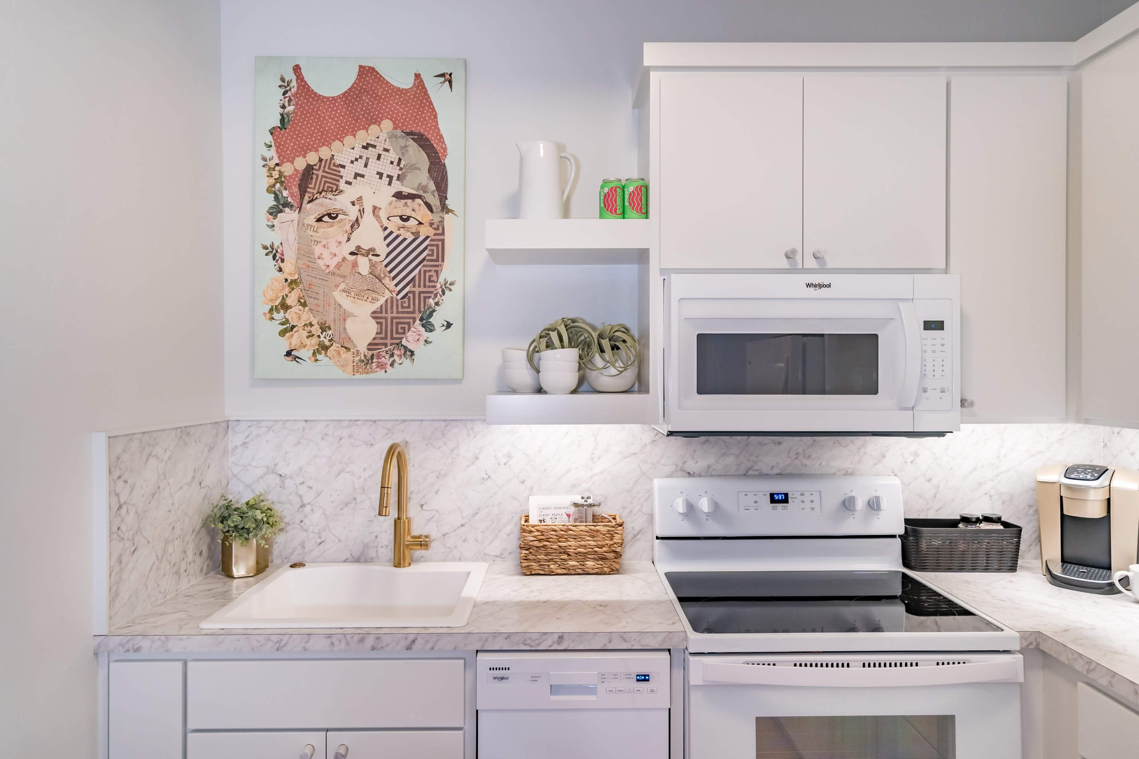 A modern kitchen features a marble countertop, white cabinetry, and a wall-mounted artwork above the sink.