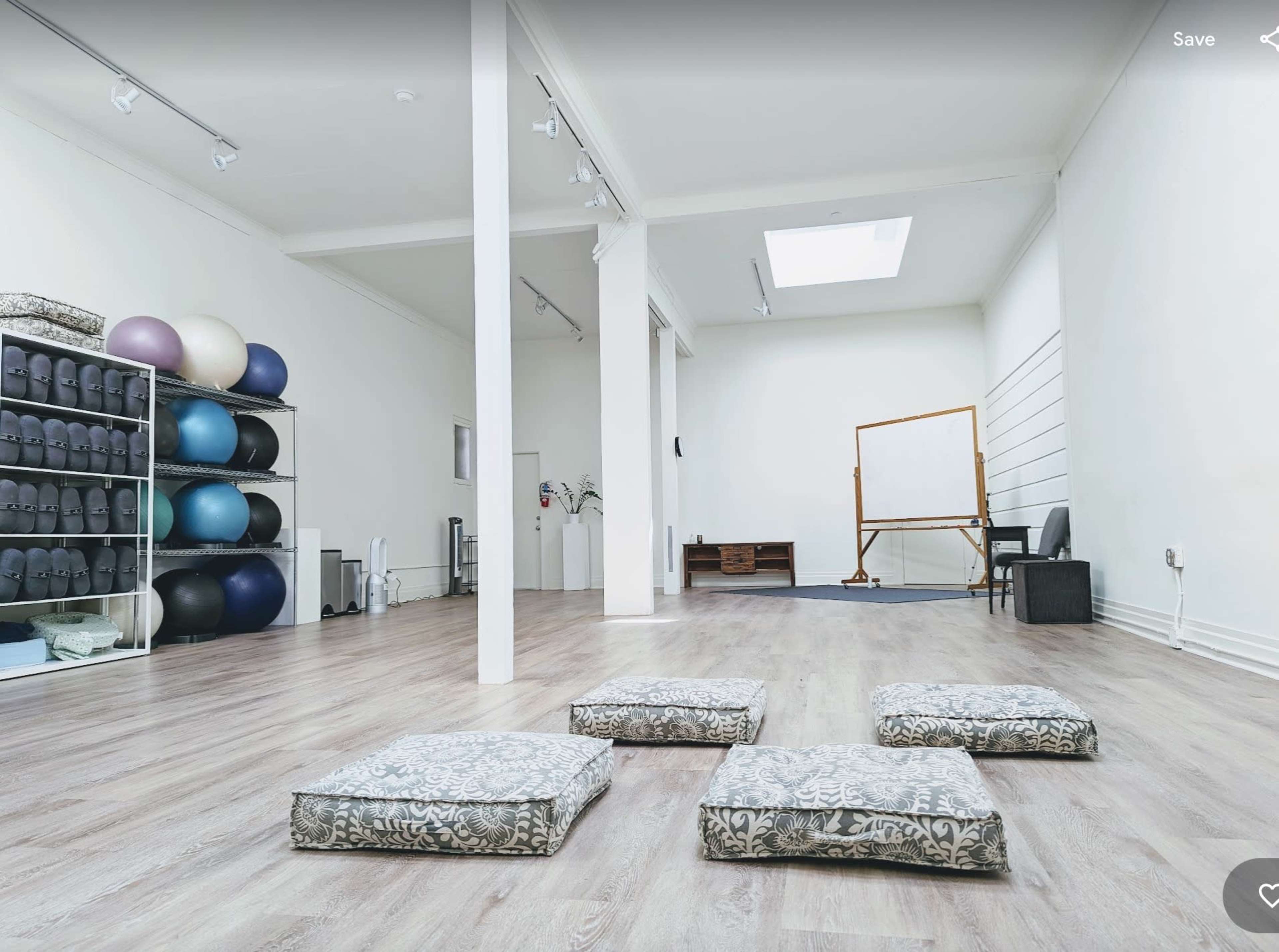 A spacious, well-lit room with exercise equipment on shelves, several cushions arranged on the floor, and a whiteboard set up against a wall.