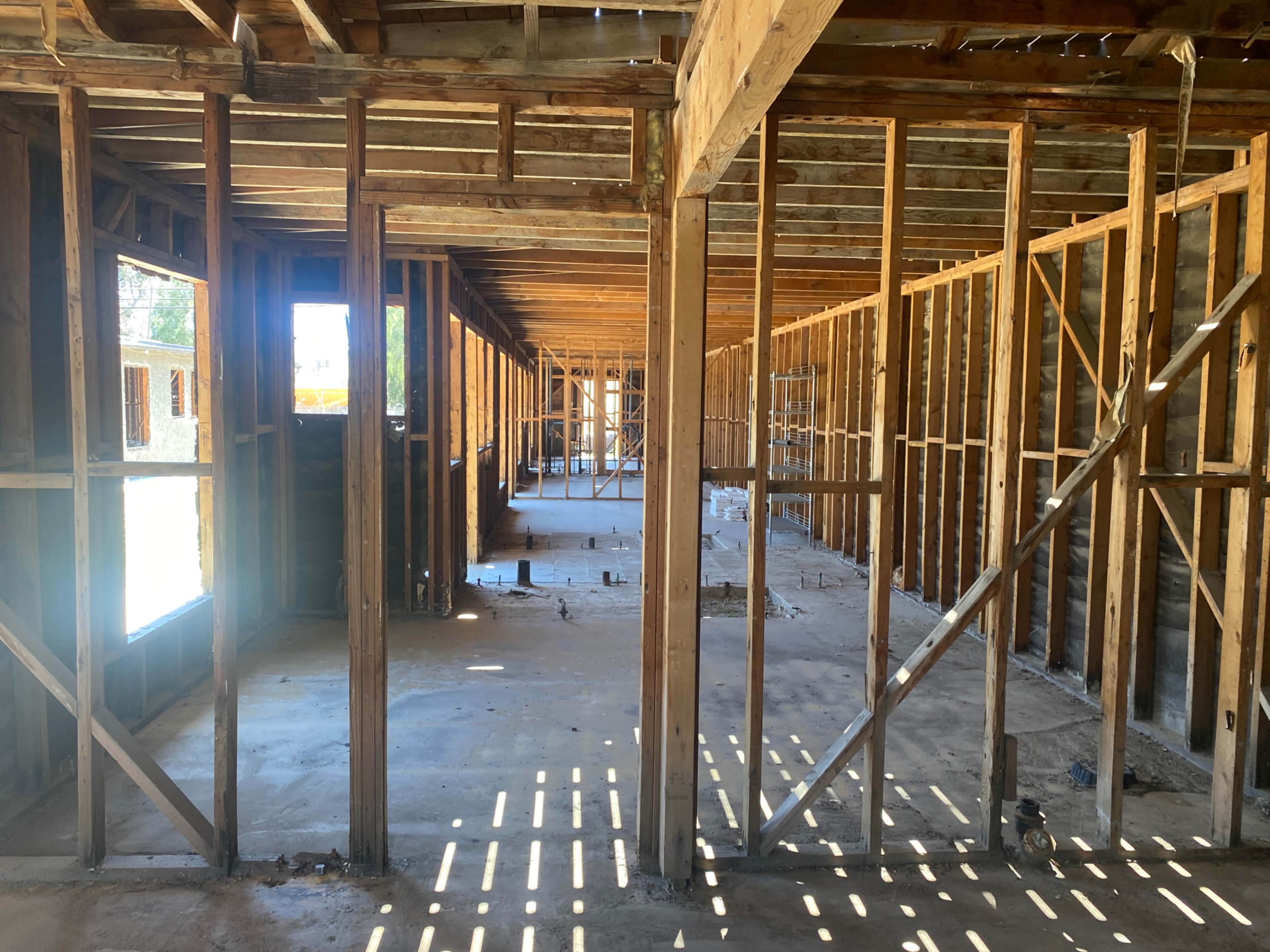 The image shows an unfinished building with exposed wooden framing and a concrete floor.