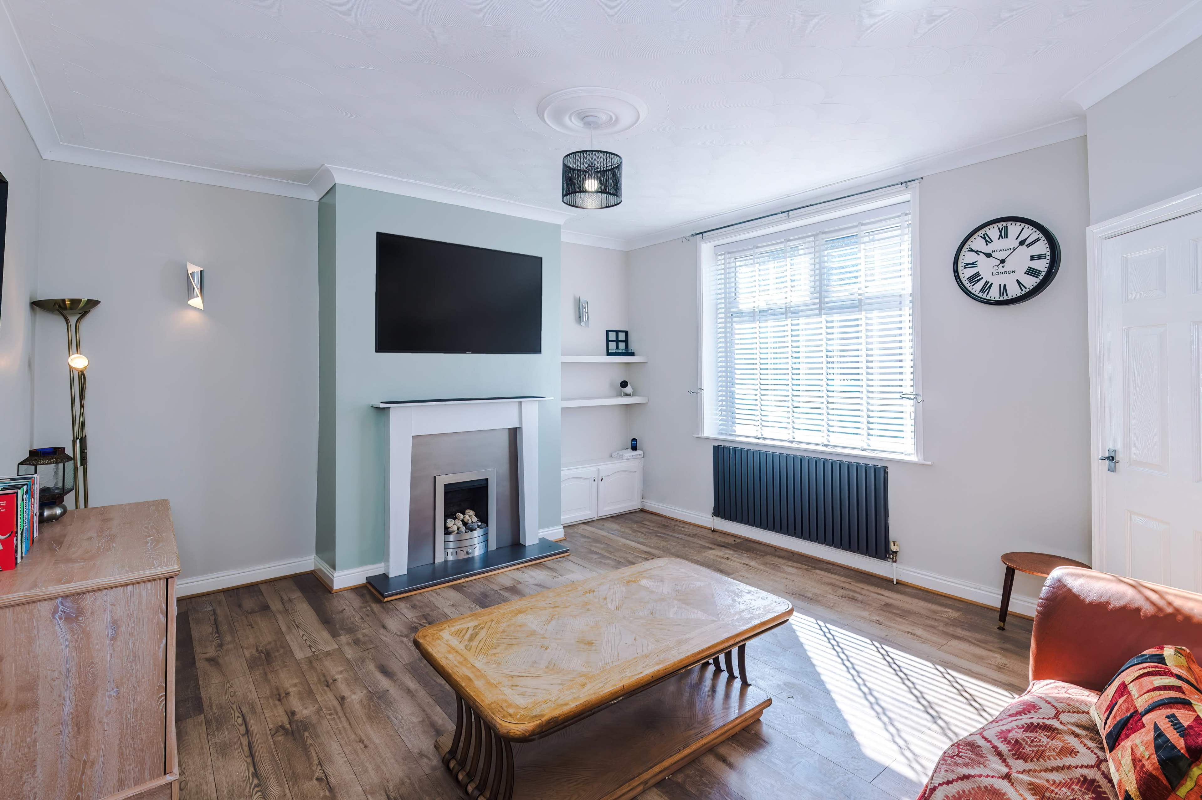 The room features a modern living area with a wooden coffee table, a flat-screen TV mounted above a fireplace, and large windows allowing natural light.