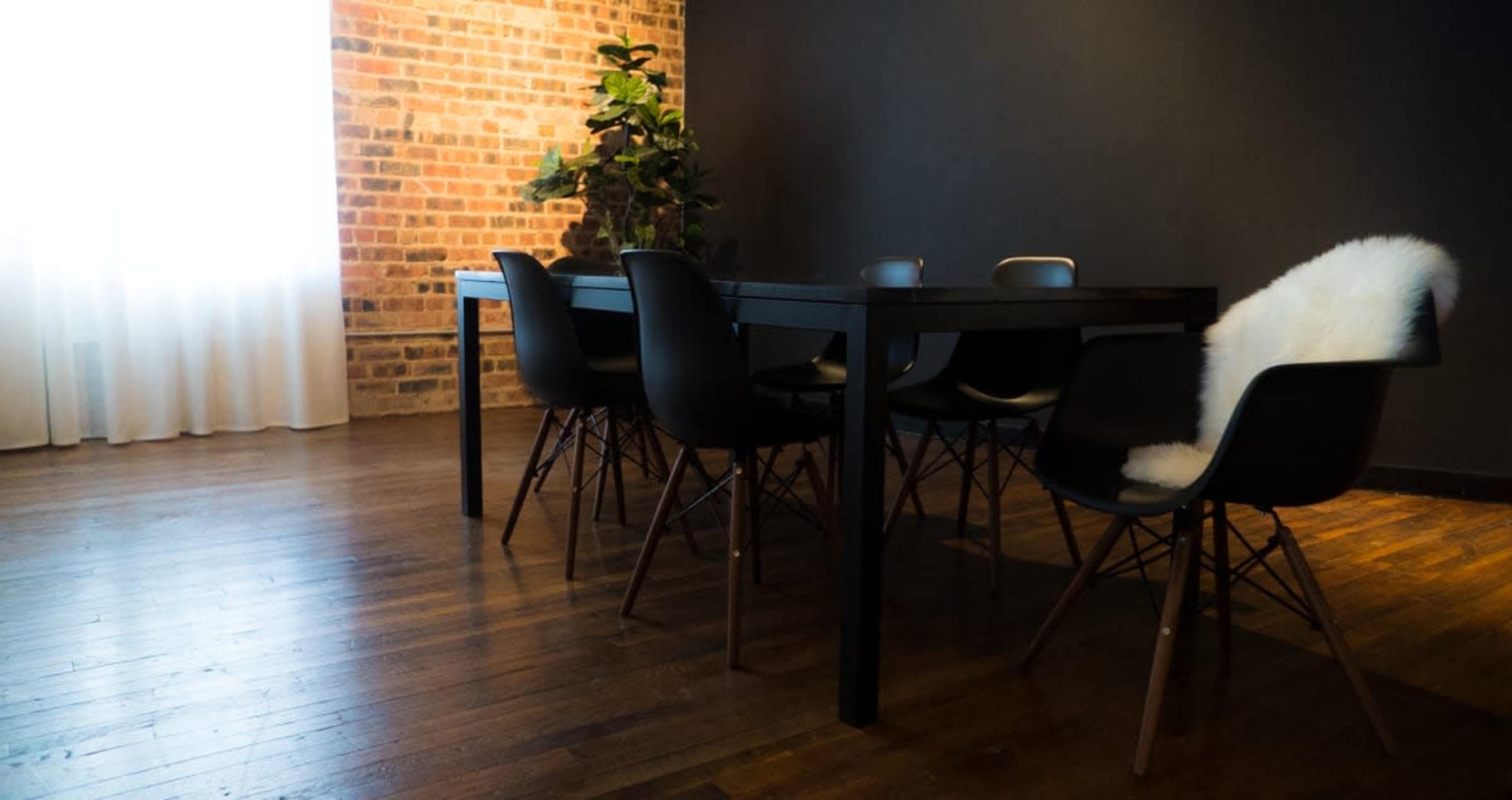 A dining area features a black table surrounded by black chairs, with a plant and a large window letting in natural light.