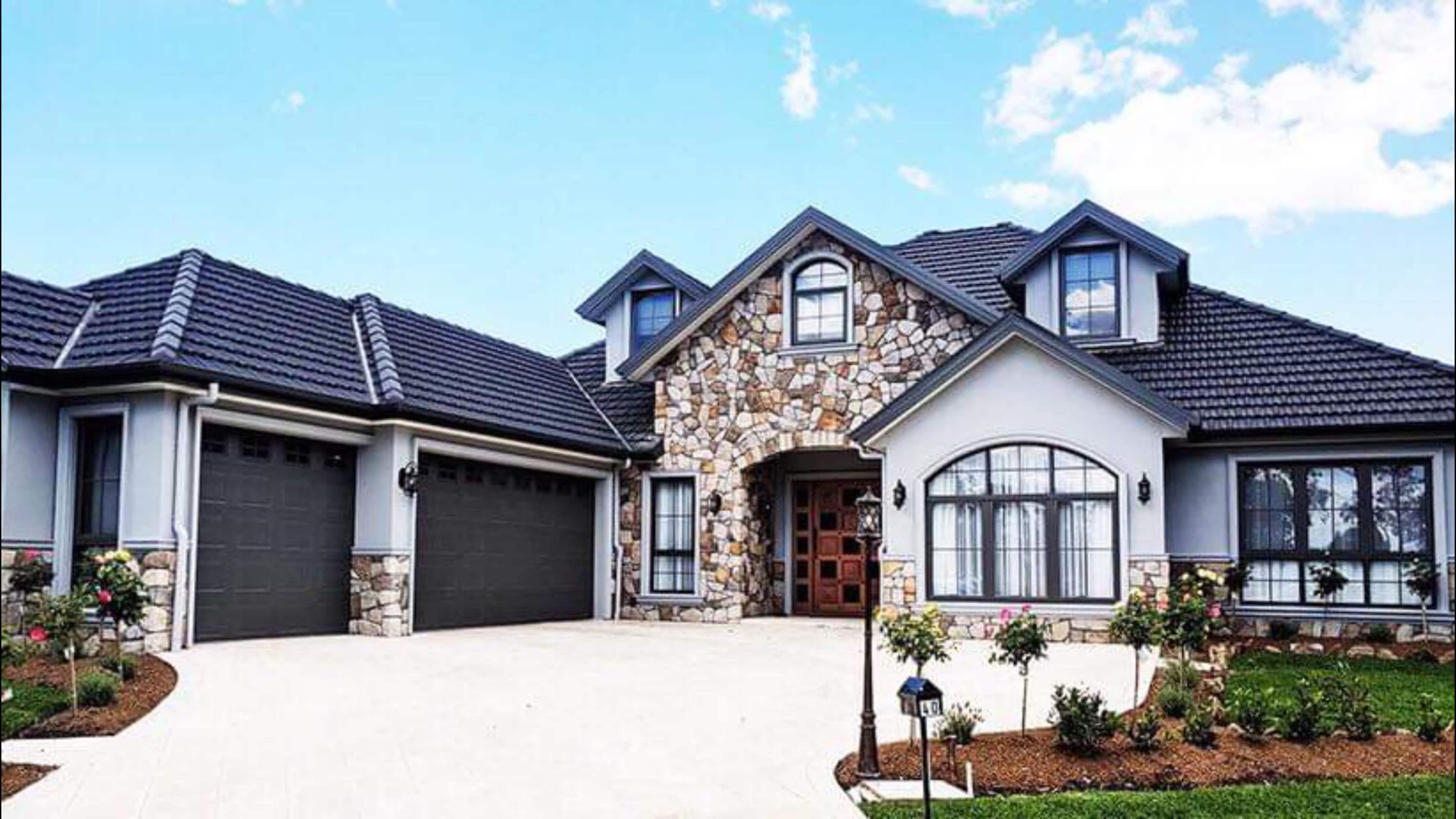 A large, modern house with a stone facade and a two-car garage, set against a clear blue sky.