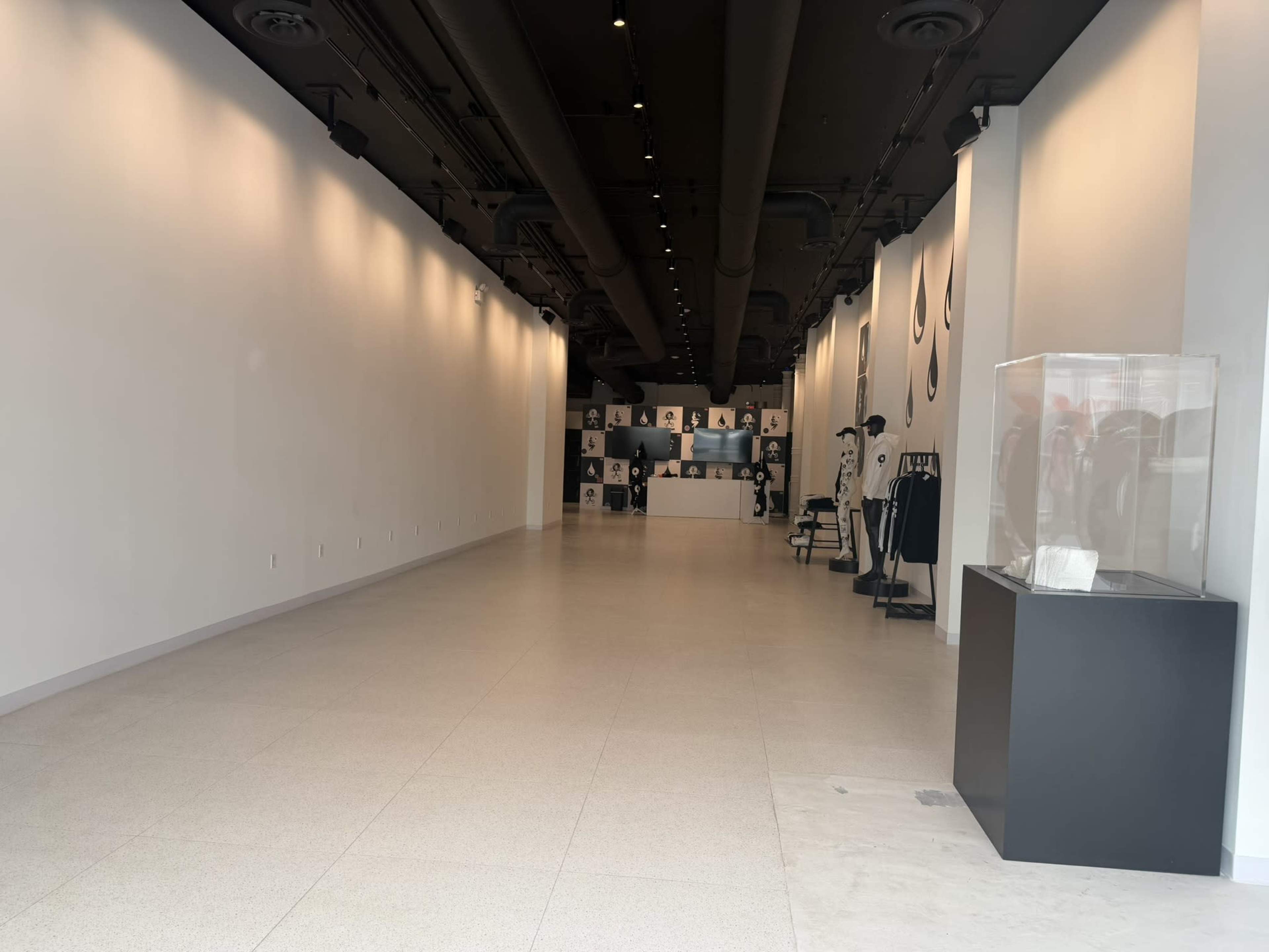 The image shows a spacious, empty retail store with white walls, a minimalist design, and displayed merchandise including clothing and accessories on the left side.