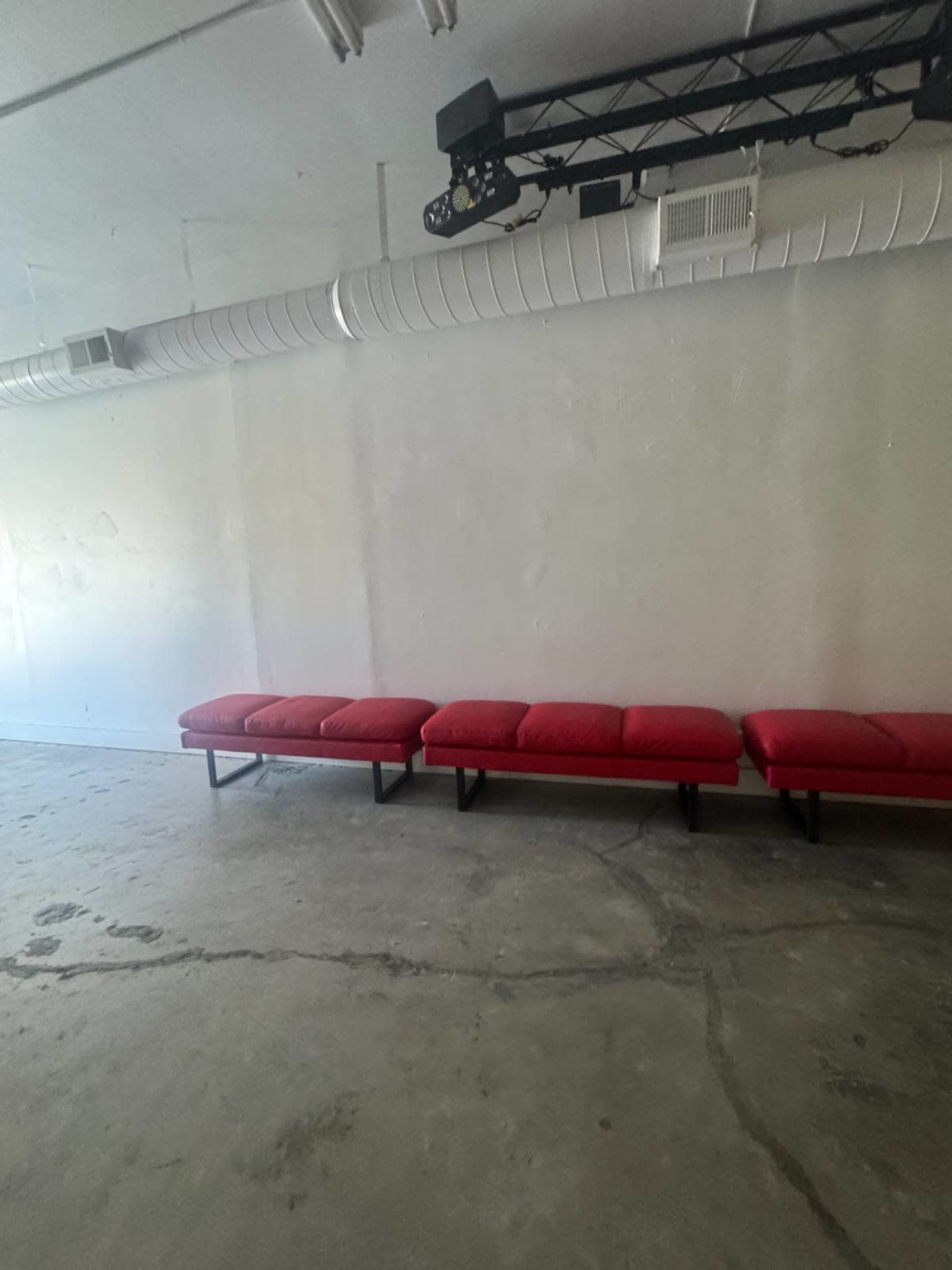 The image shows a stark room with a row of red benches against a plain white wall.