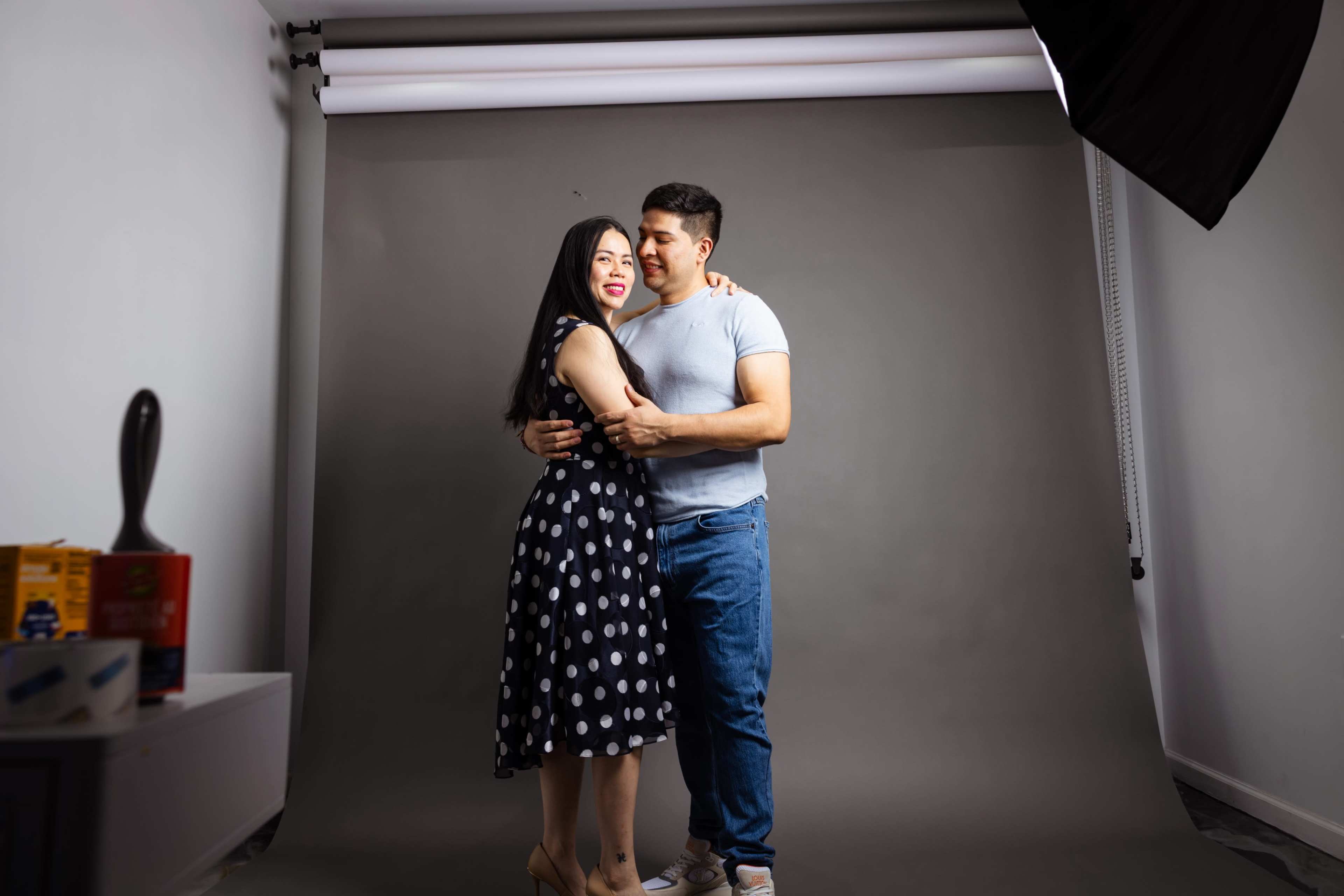 A couple embraces in a photography studio with a neutral gray backdrop.