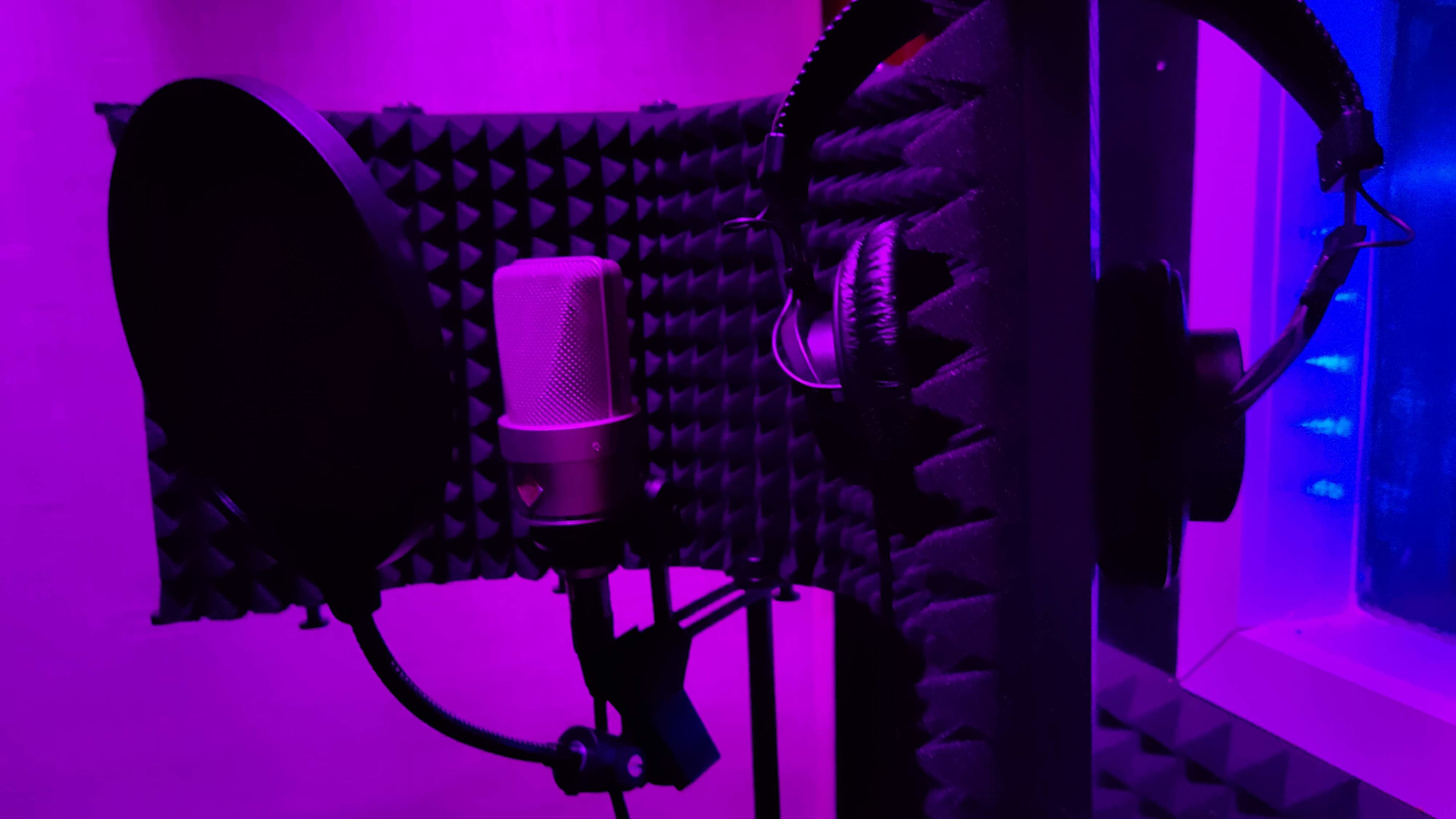 The image shows a recording studio setup with a microphone and headphones set against a backdrop of acoustic panels illuminated by purple lighting.