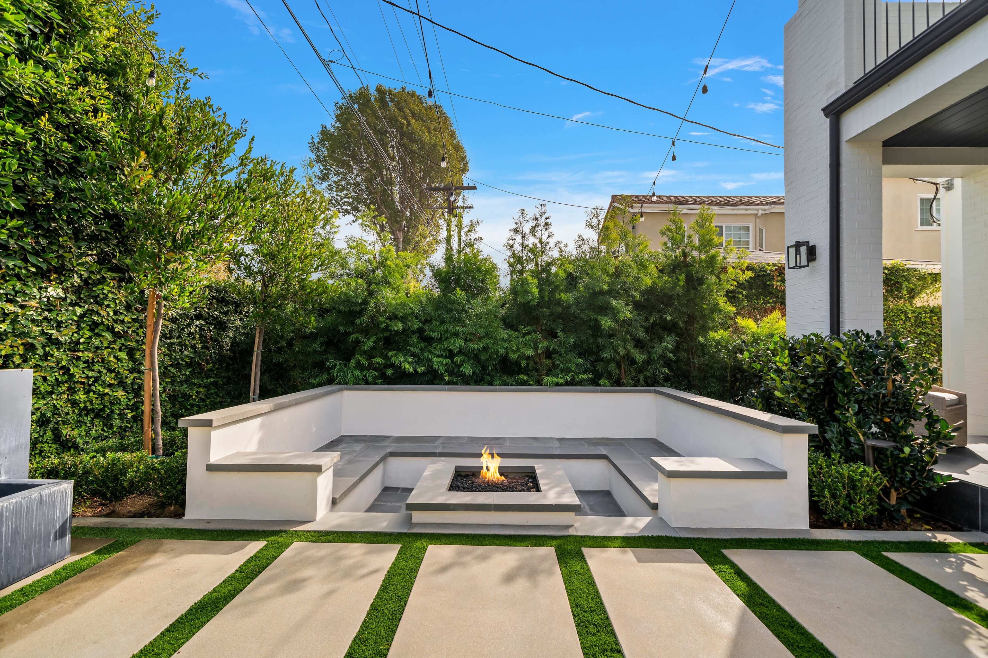 A modern outdoor seating area with a fire pit surrounded by low stone walls and neatly manicured grass pathways.