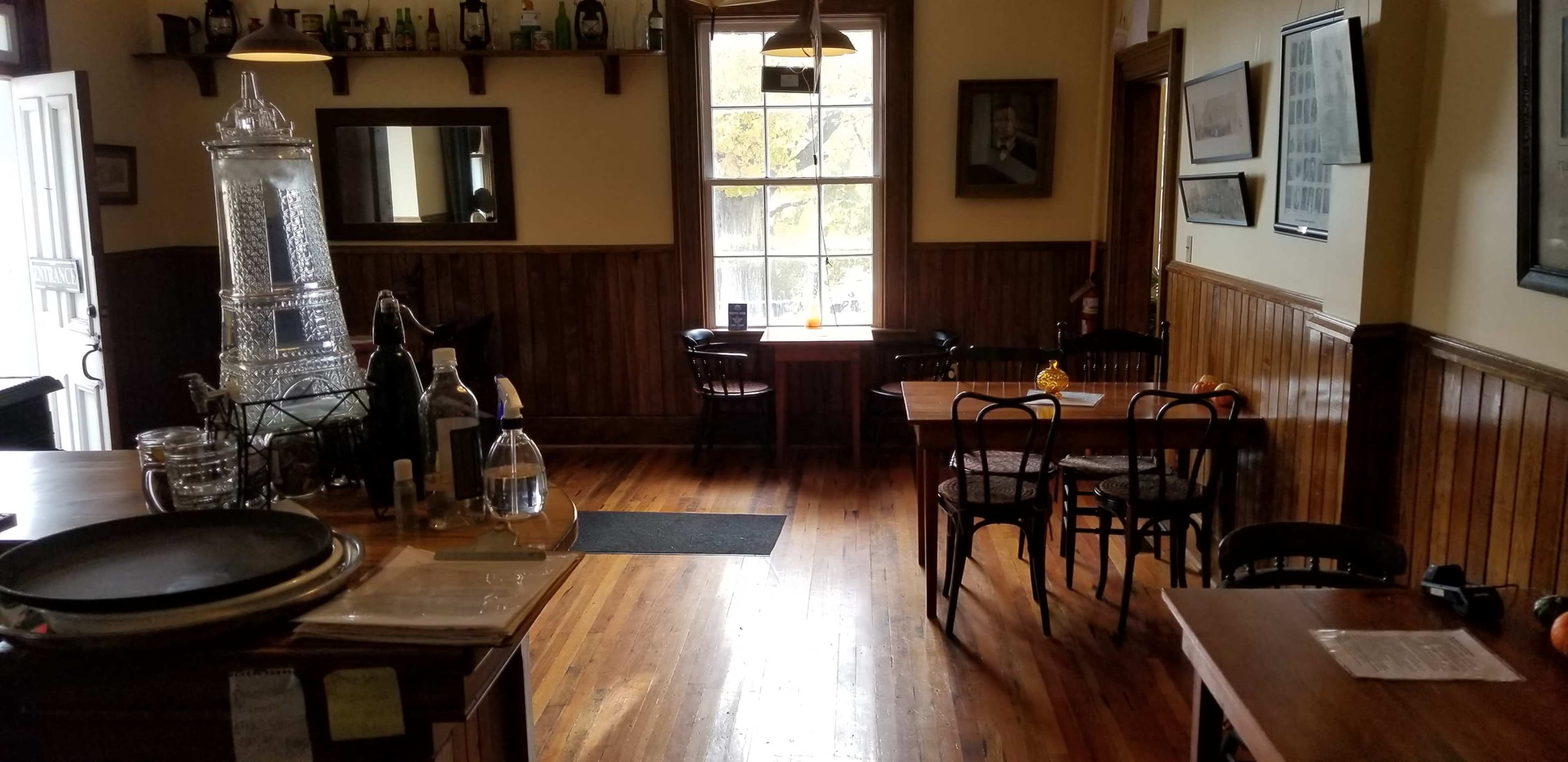 A rustic interior of a restaurant with wooden walls, a bar area on the left, and several tables arranged in the dining area.