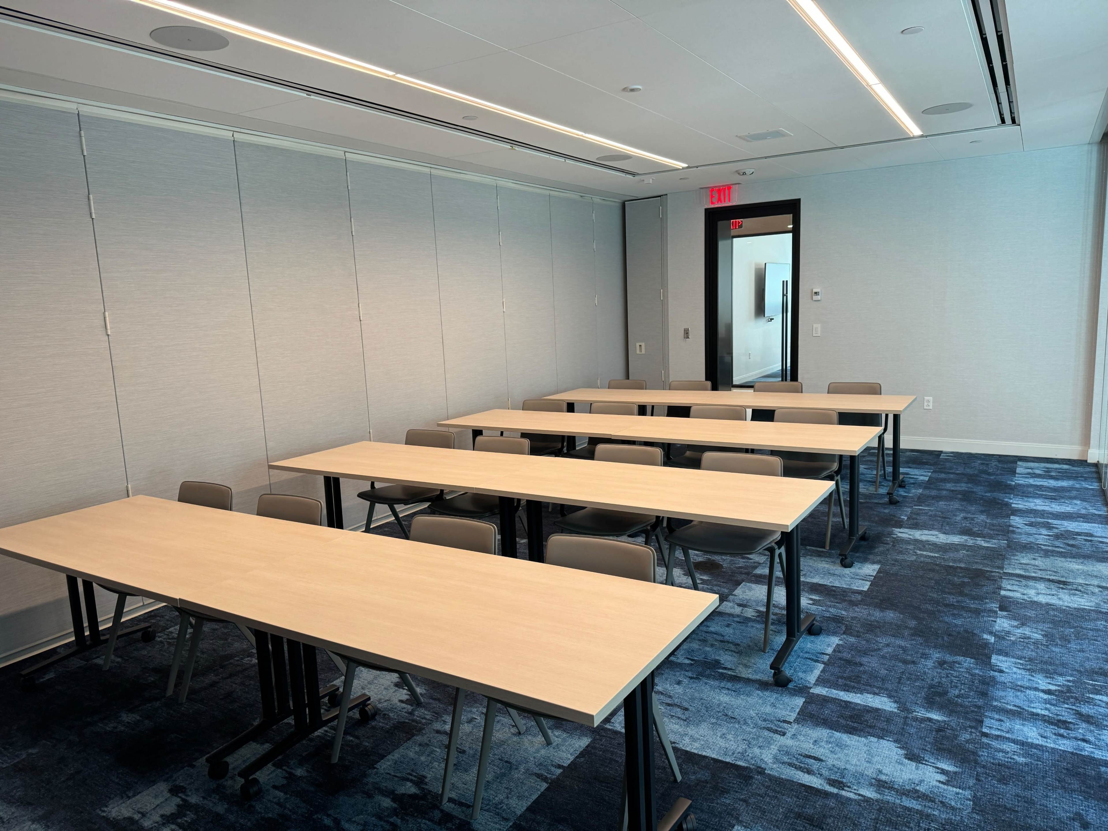 A modern conference room with several tables arranged in rows and a blue carpeted floor.