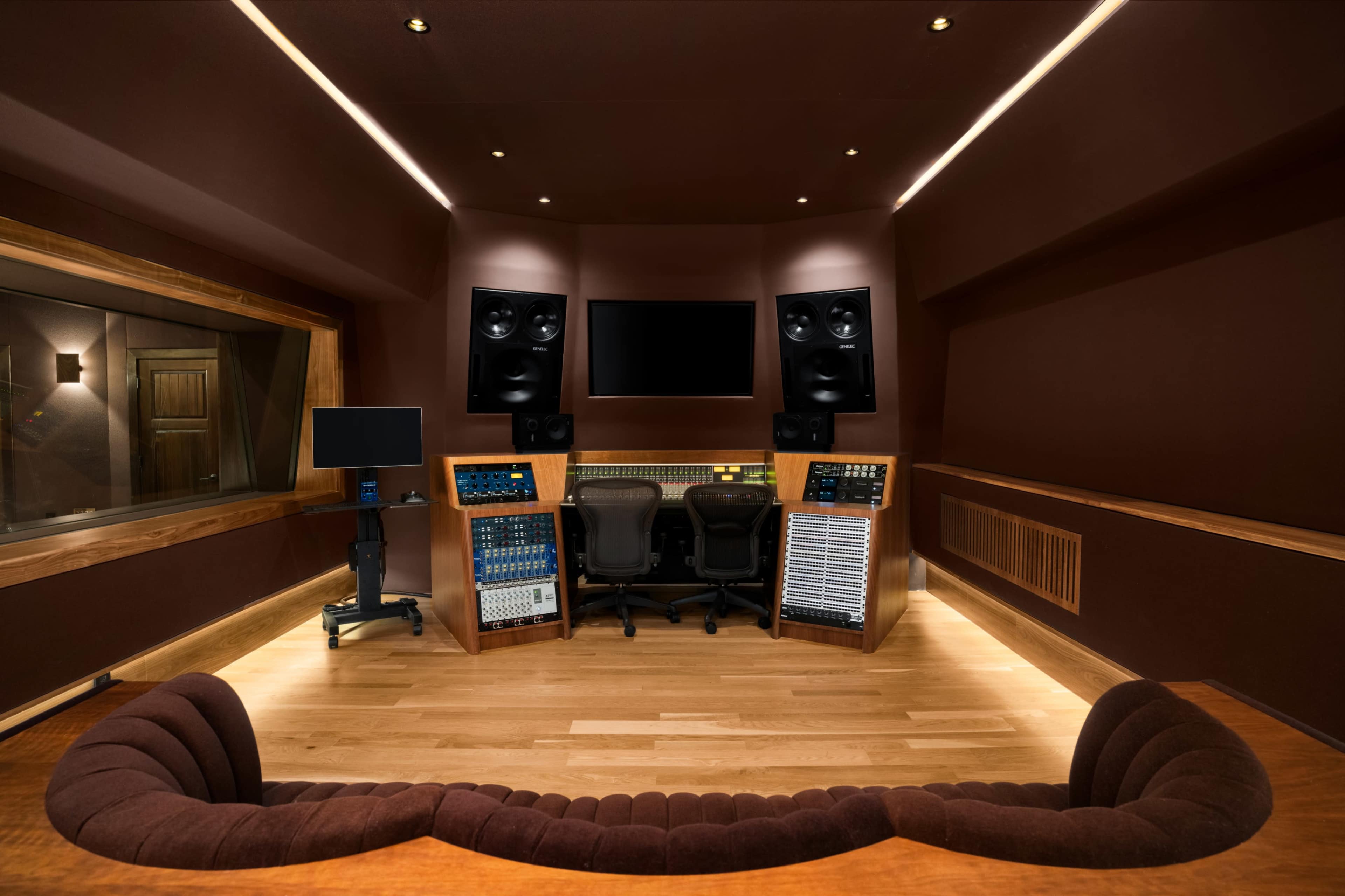 The image shows a modern audio recording studio featuring mixing consoles, large speakers, and a comfortable seating area.