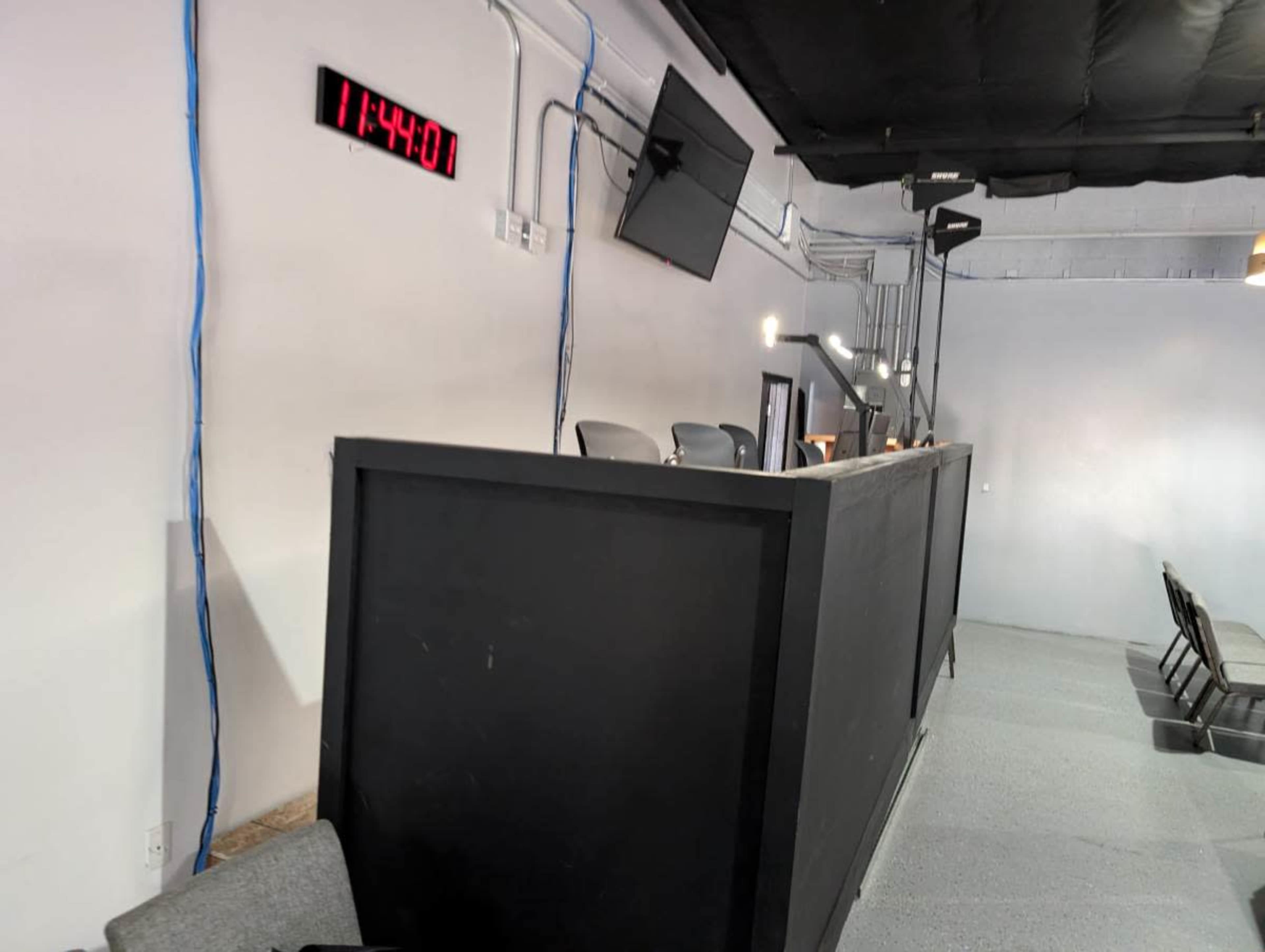 The image shows a dimly lit room with a large digital timer displaying 11:44:00 and a series of chairs in the foreground.