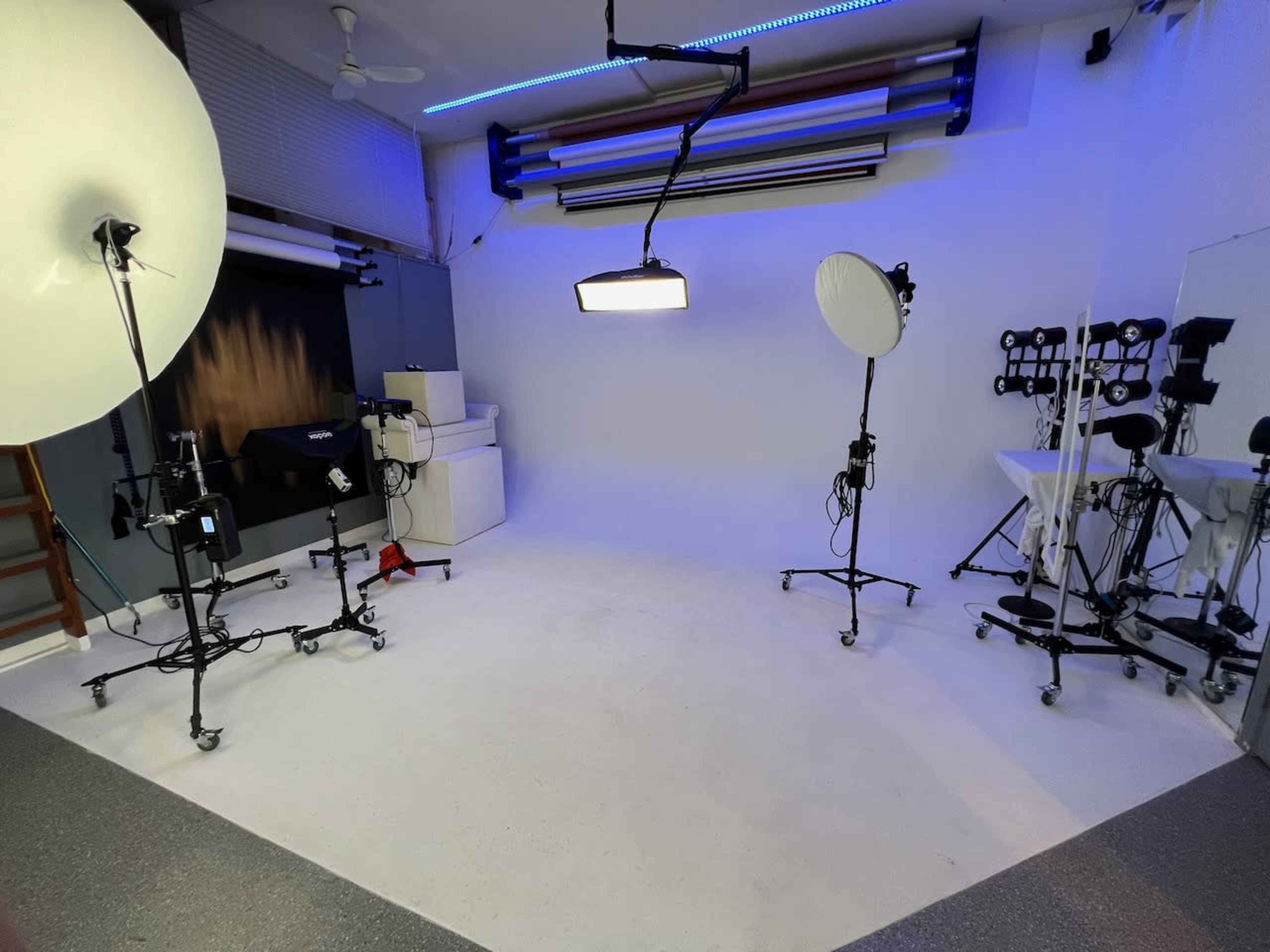 A photography studio with various lighting equipment and a plain backdrop.