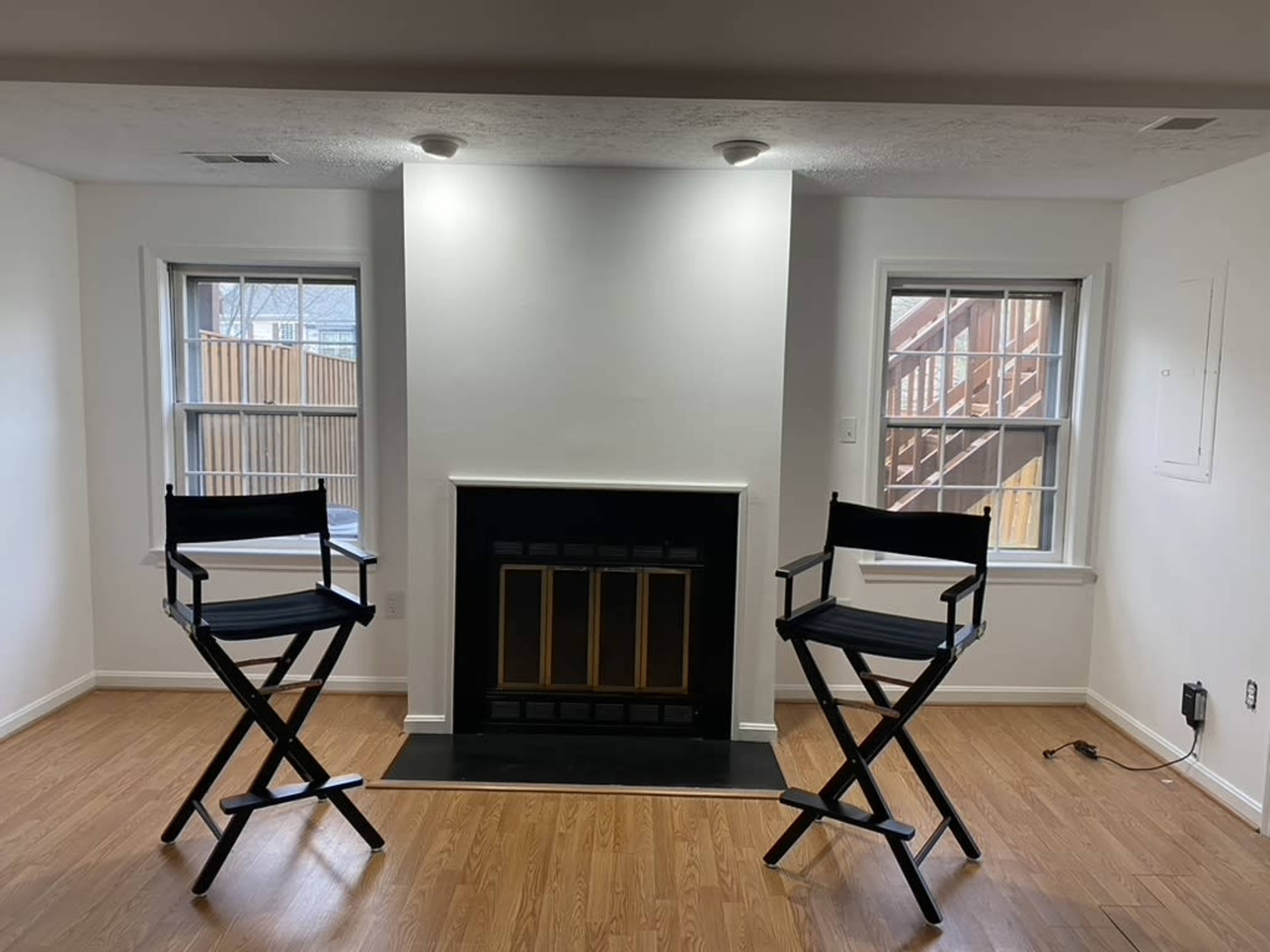 A room with two director's chairs positioned in front of a black fireplace, flanked by two windows.