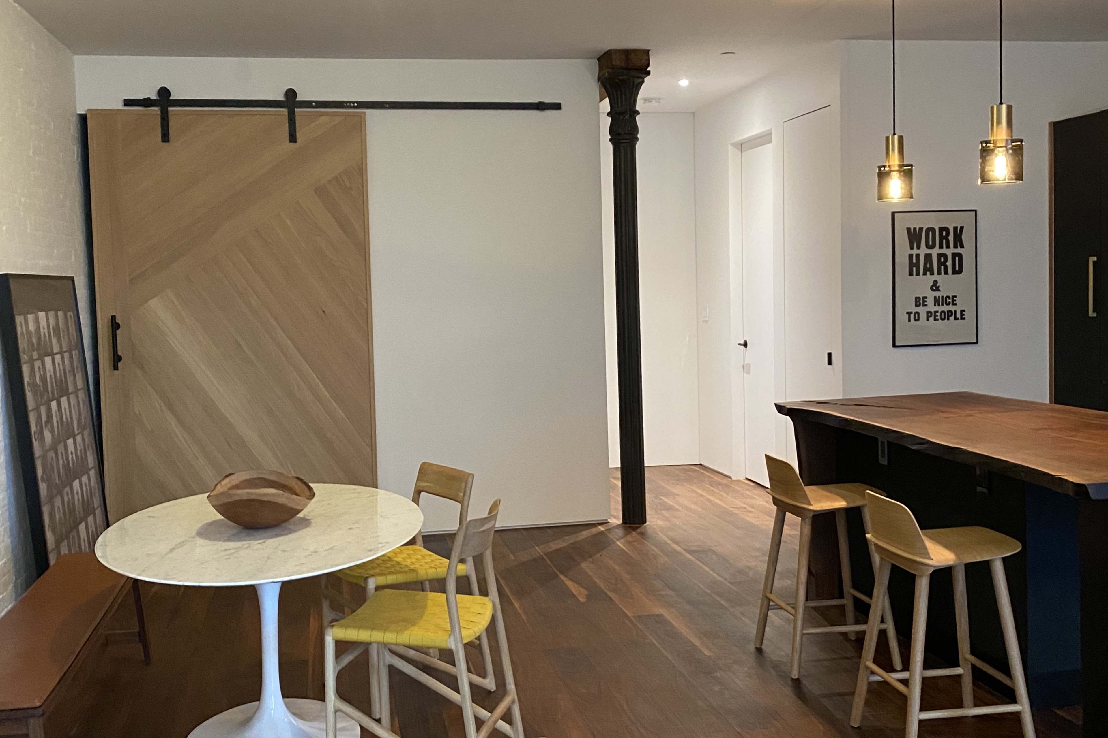 A modern interior space with a circular dining table, wooden chairs, a sliding door, and a kitchen bar area with pendant lighting.