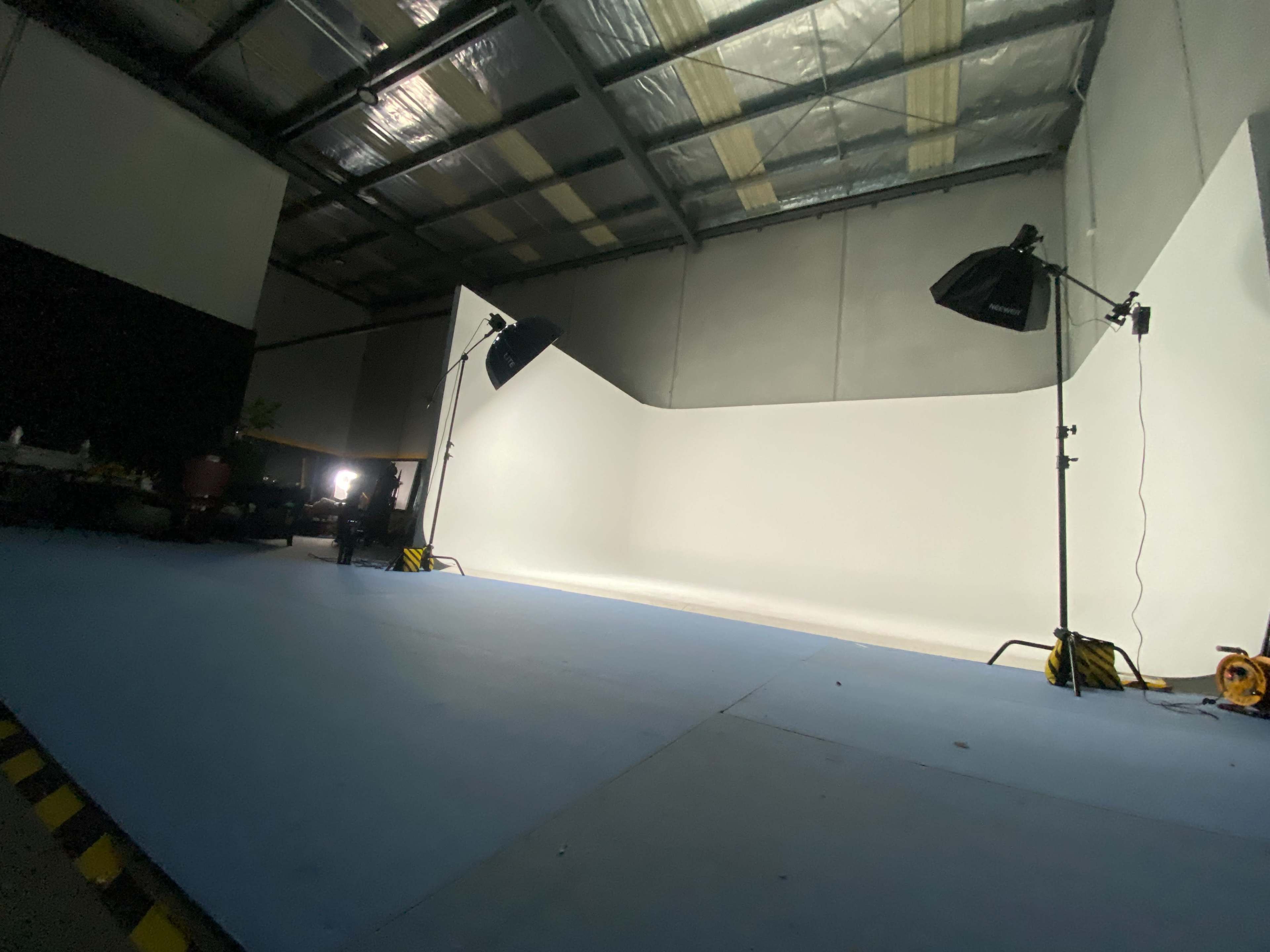 A photography studio with a curved white backdrop, two lighting setups, and a blue floor.
