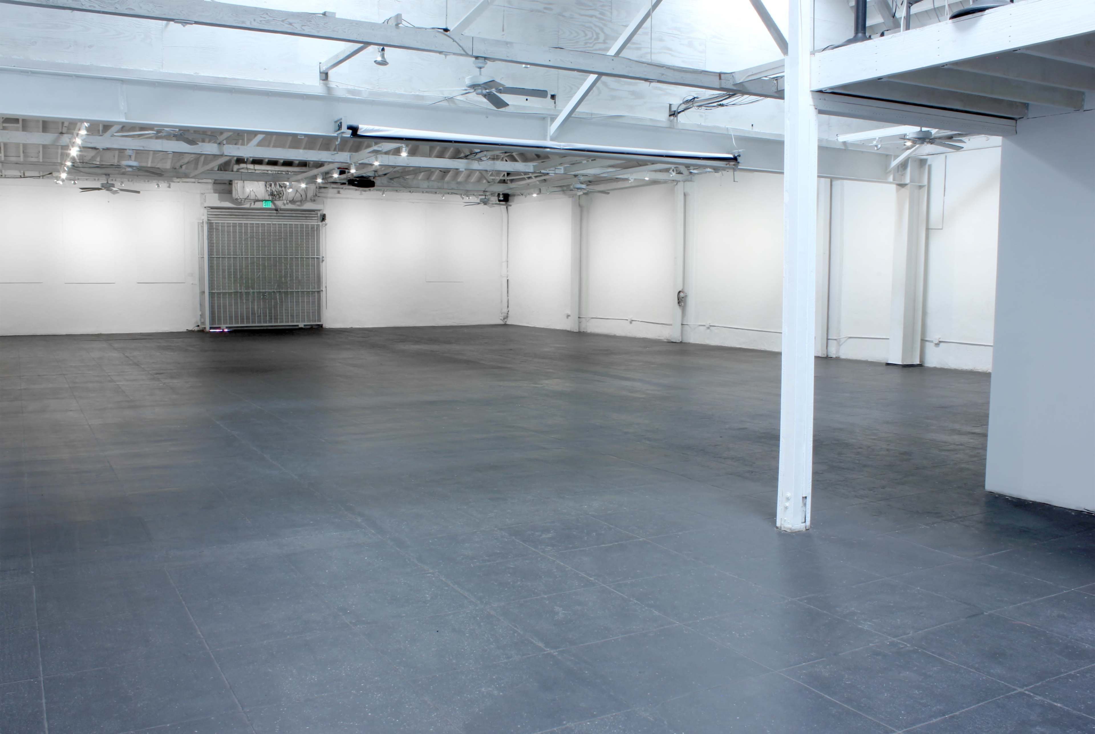 The image shows a large, empty warehouse space with a concrete floor and white walls.