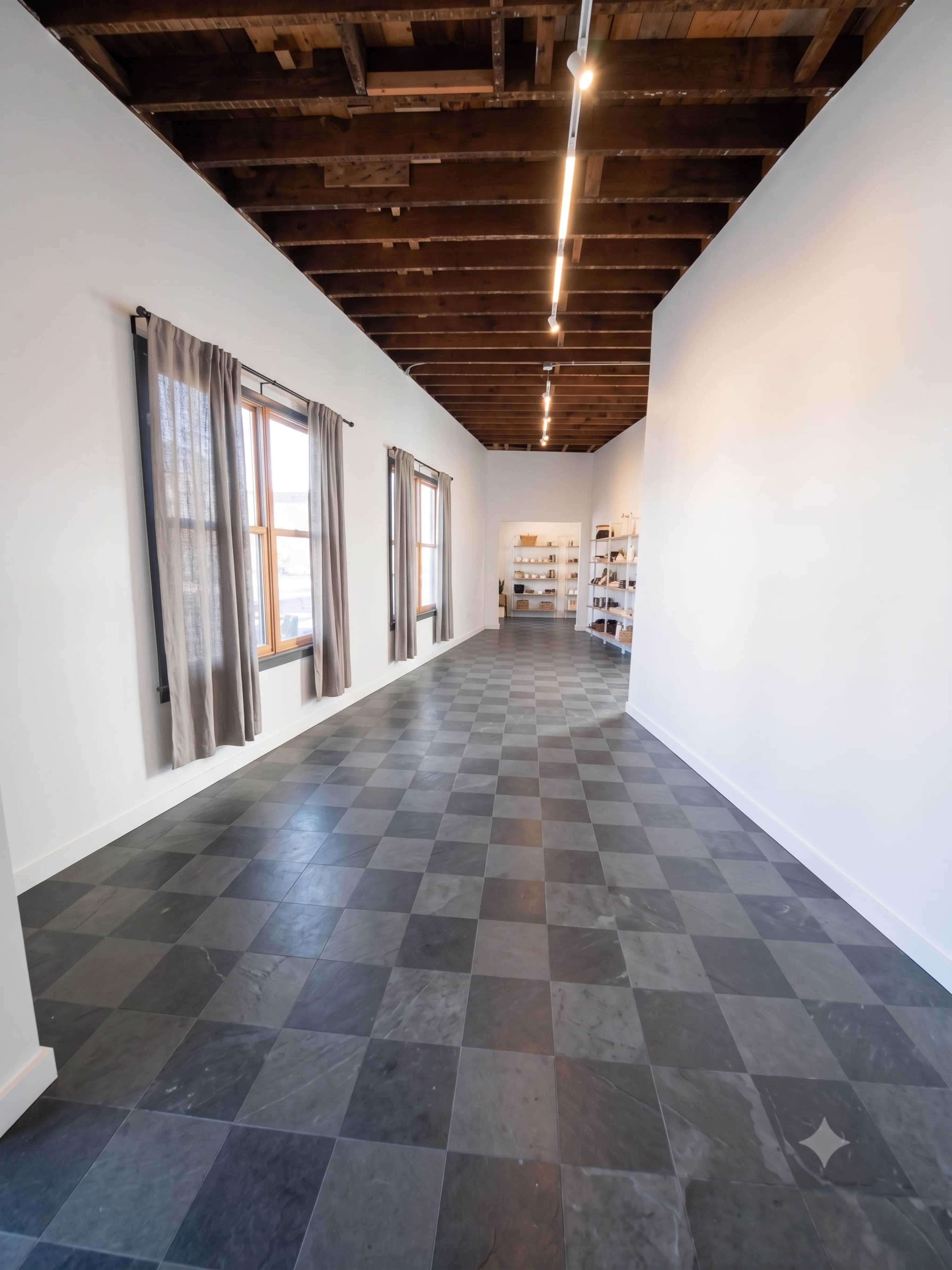 The image shows a narrow, well-lit hallway with a checkered floor, large windows on one side, and shelves along the wall at the far end.