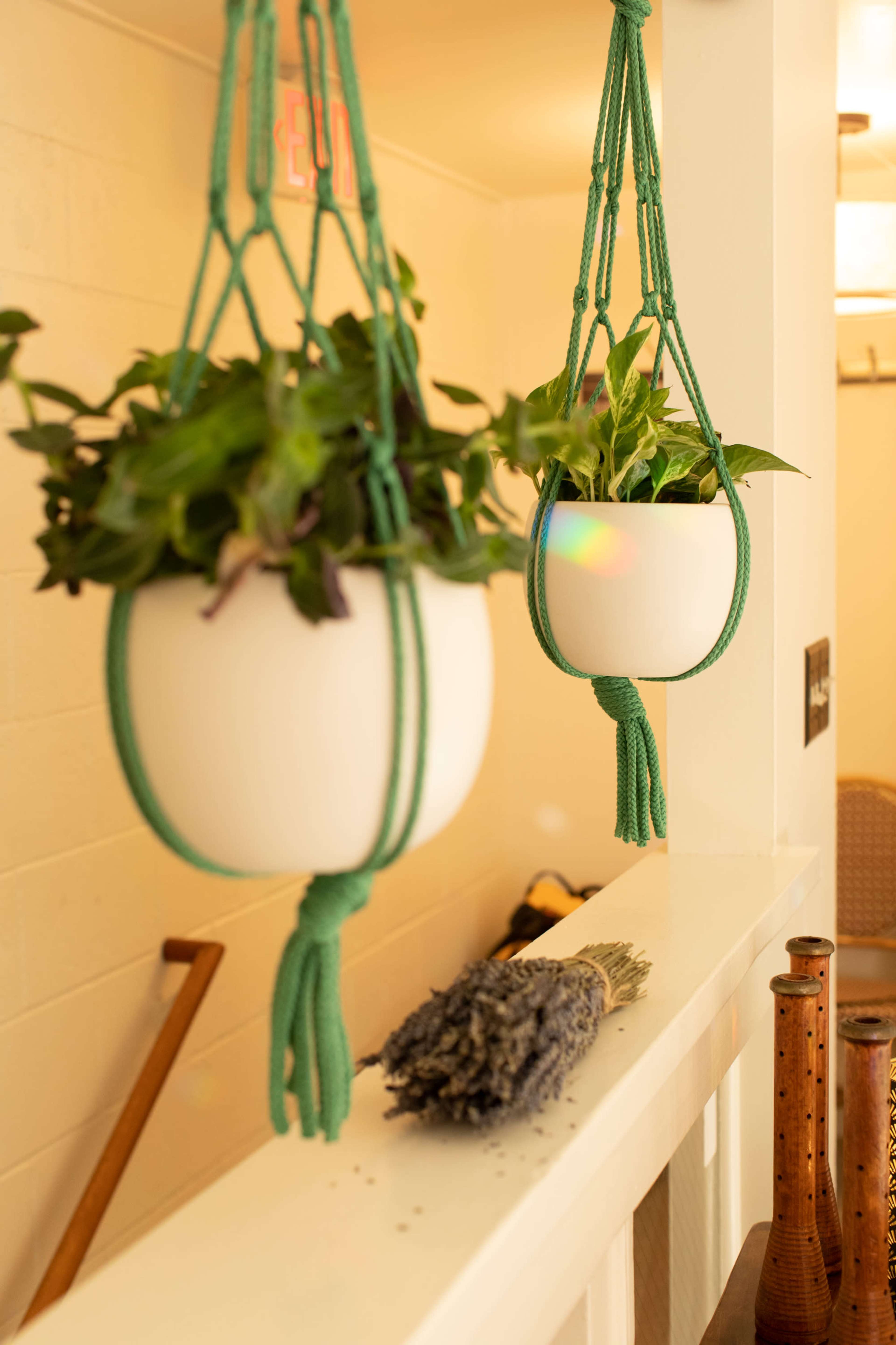 Two hanging planters with green plants are suspended from a wall, accompanied by a bundle of lavender placed on a ledge nearby.
