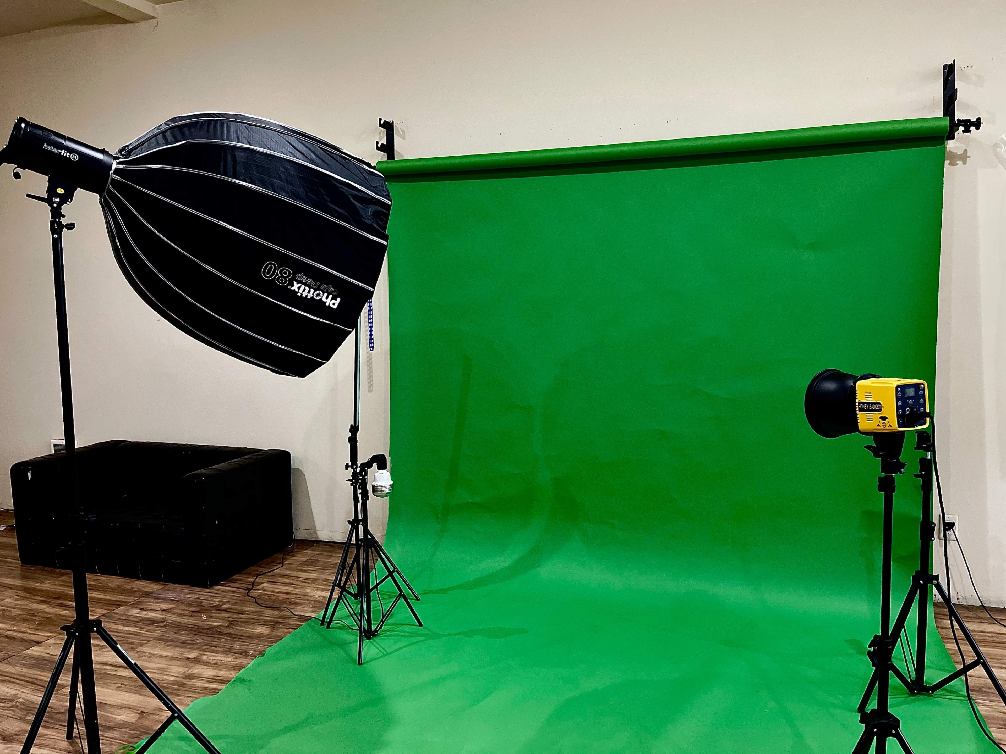 A photography studio setup featuring a green backdrop, a softbox light on the left, and a strobe light on the right.