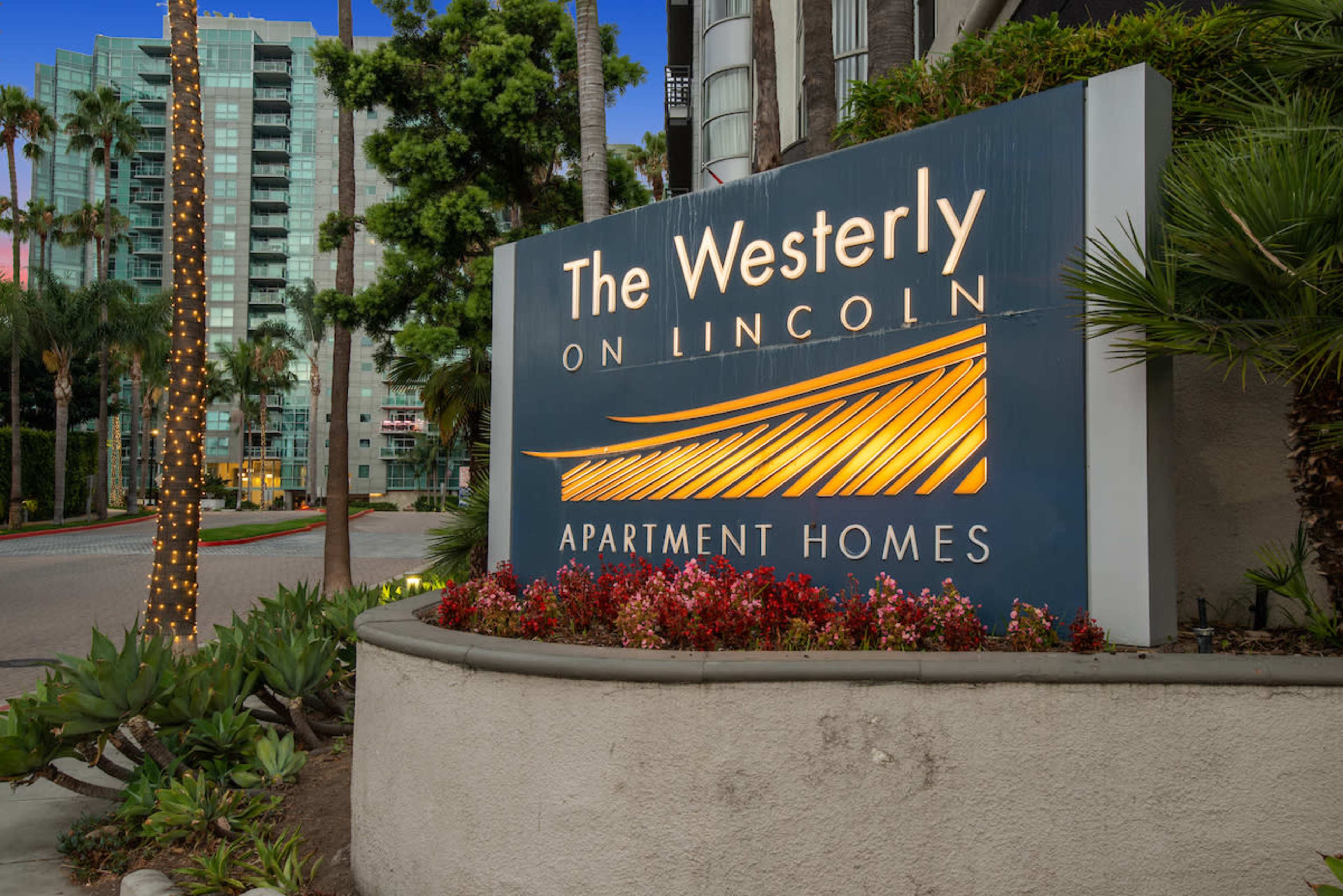 The illuminated sign for "The Westerly on Lincoln Apartment Homes," surrounded by palm trees and landscaping.