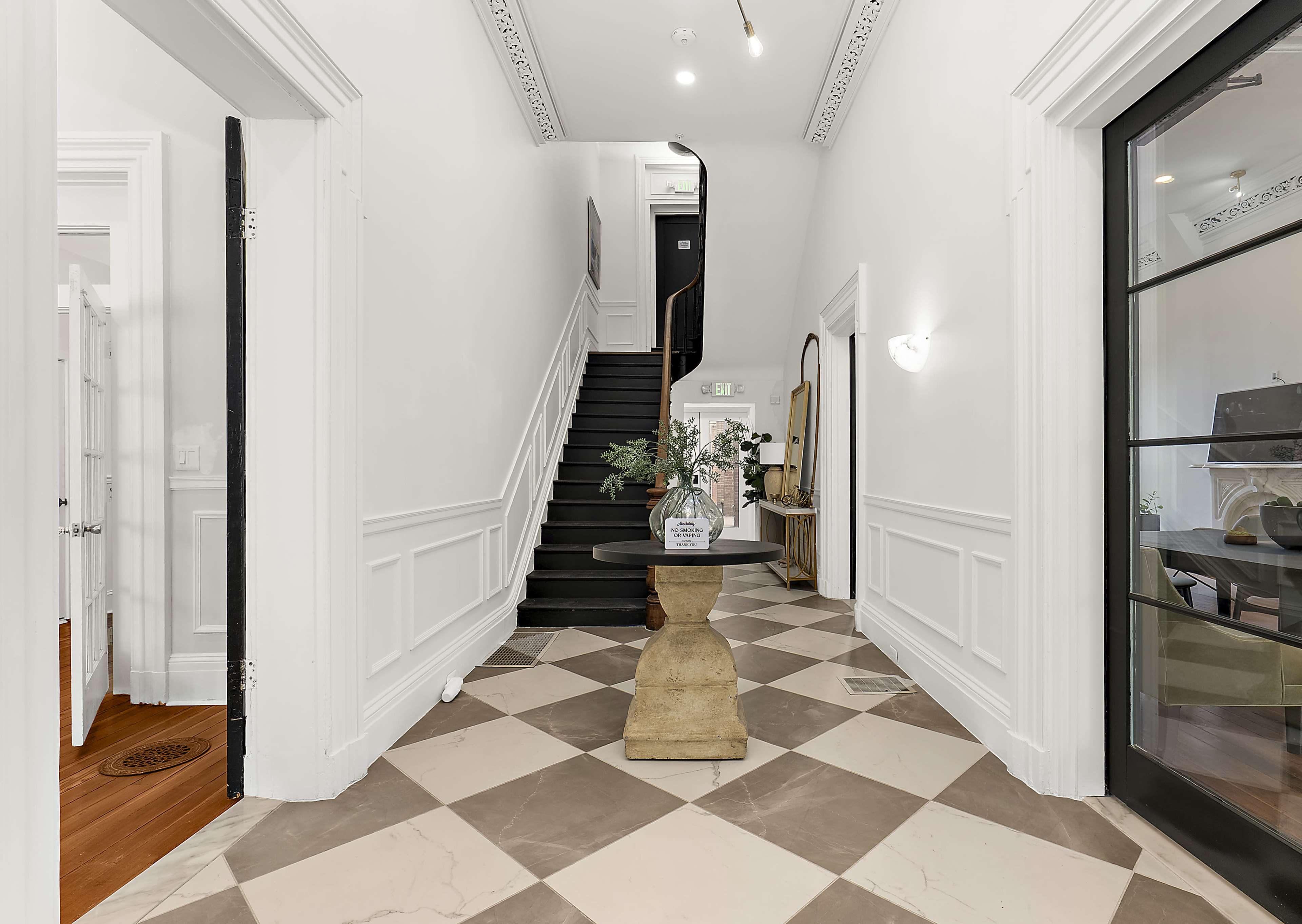 The image shows a spacious entryway featuring a black staircase, a decorative table in the center, and patterned tile flooring.