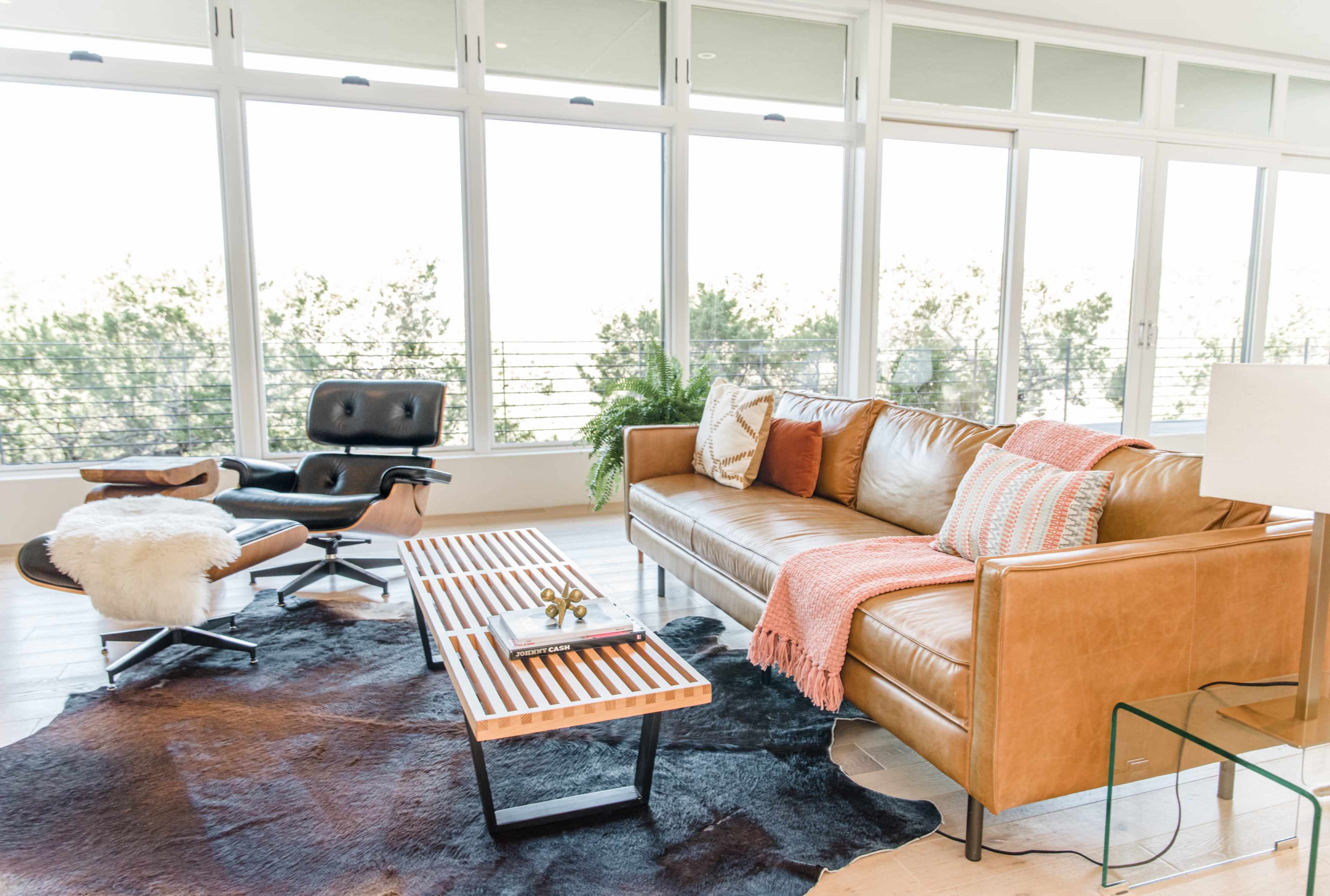 A modern living room with a leather sofa, a wooden coffee table, a decorative throw, and large windows allowing natural light.