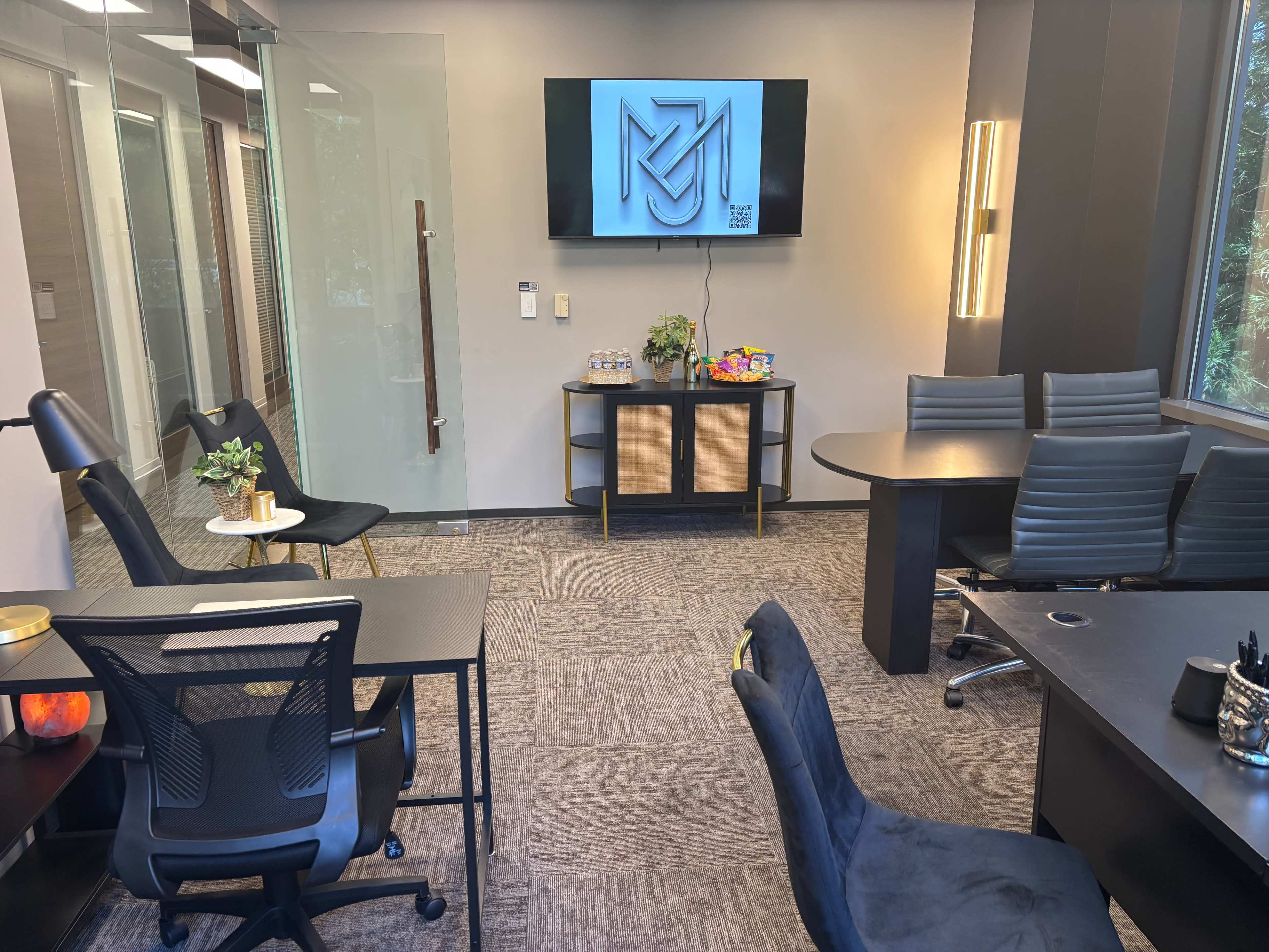 The image shows a modern office meeting room featuring a large screen, a conference table with chairs, and various plants decoratively placed.