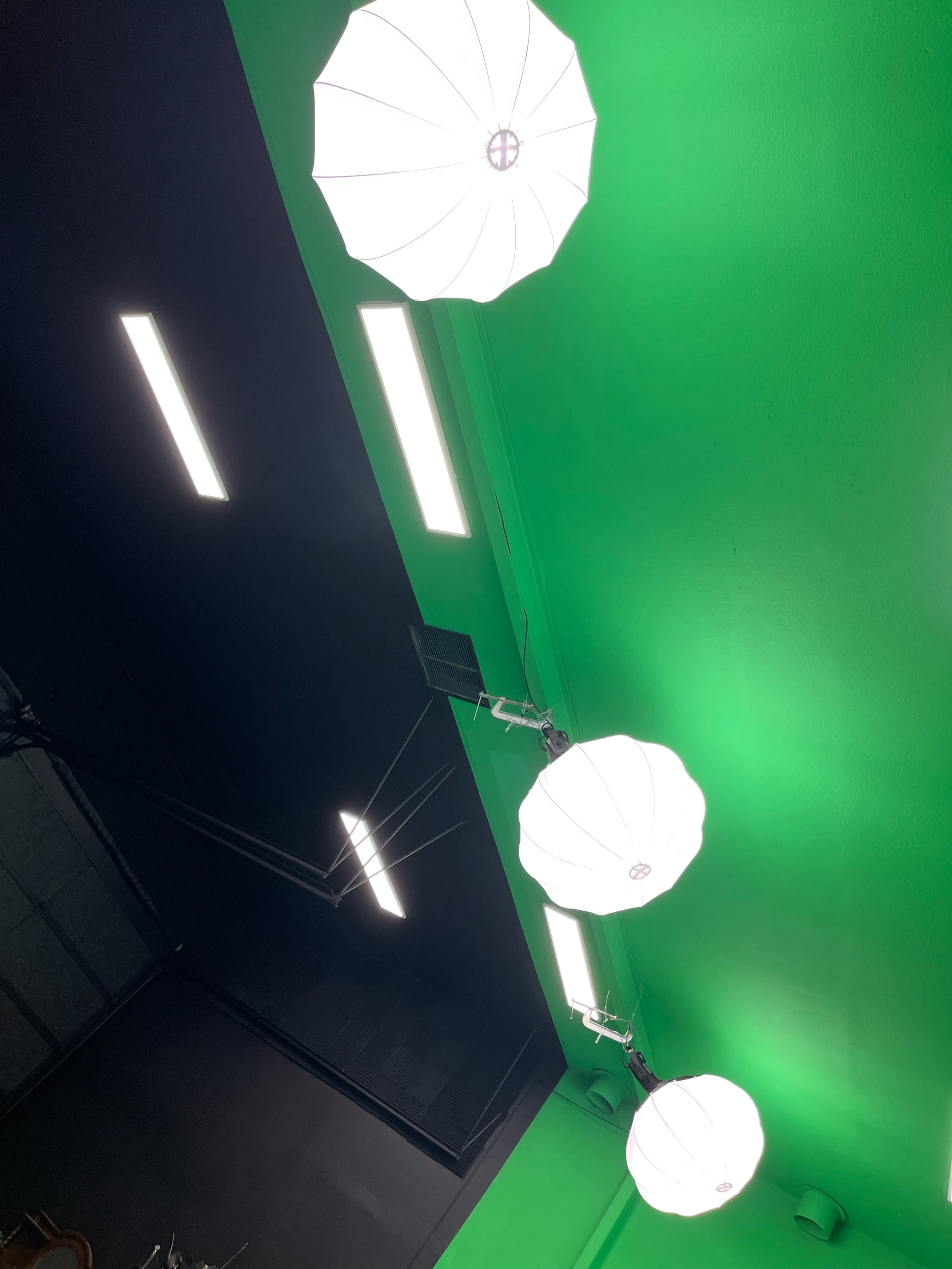 Three large umbrella lights mounted on the ceiling, illuminating a green wall alongside fluorescent light fixtures.